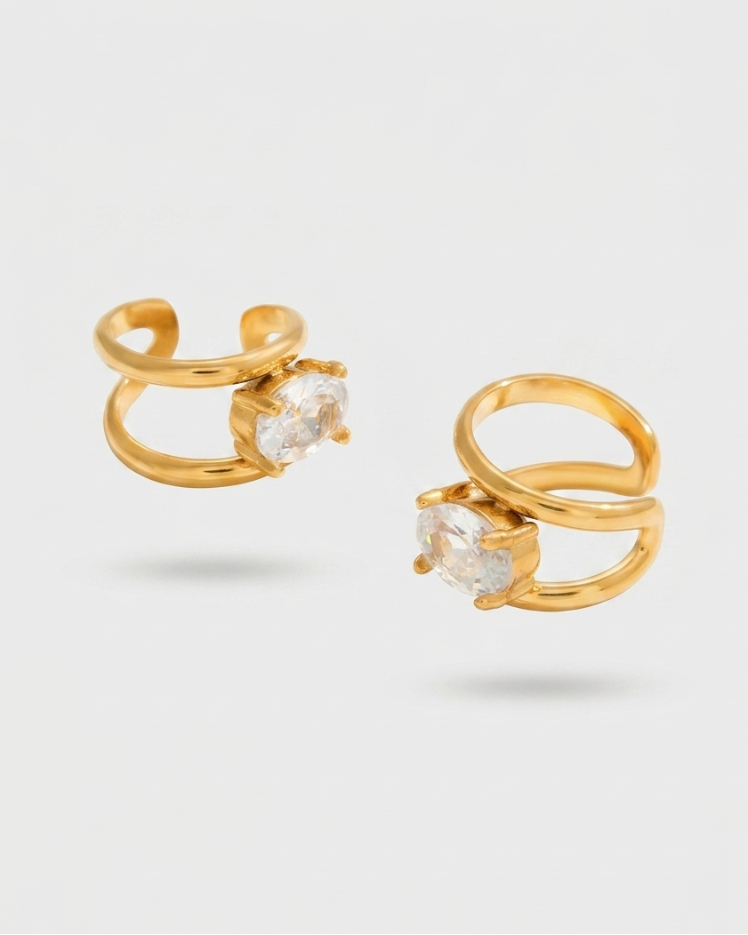 Gold open-style earrings with clear gemstones on a light gray background