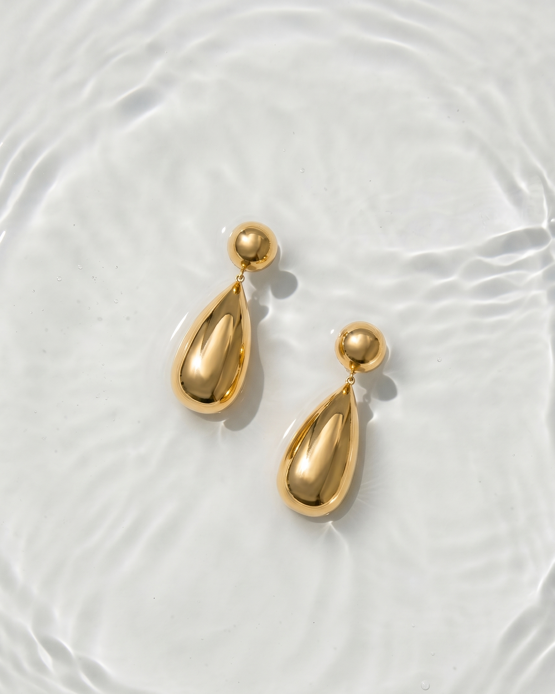 Gold teardrop earrings on a white textured surface