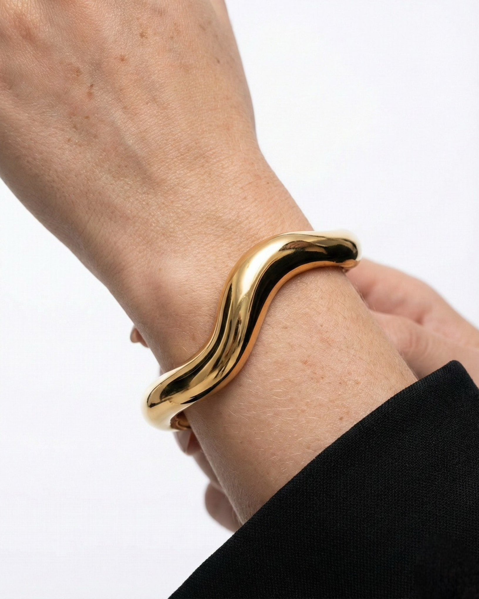 Gold bracelet on a wrist against a white background