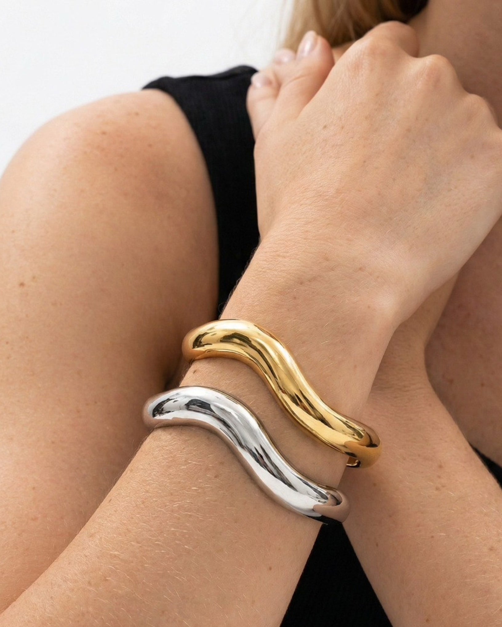 Two bracelets, one gold and one silver, on a person's wrist against a neutral background.