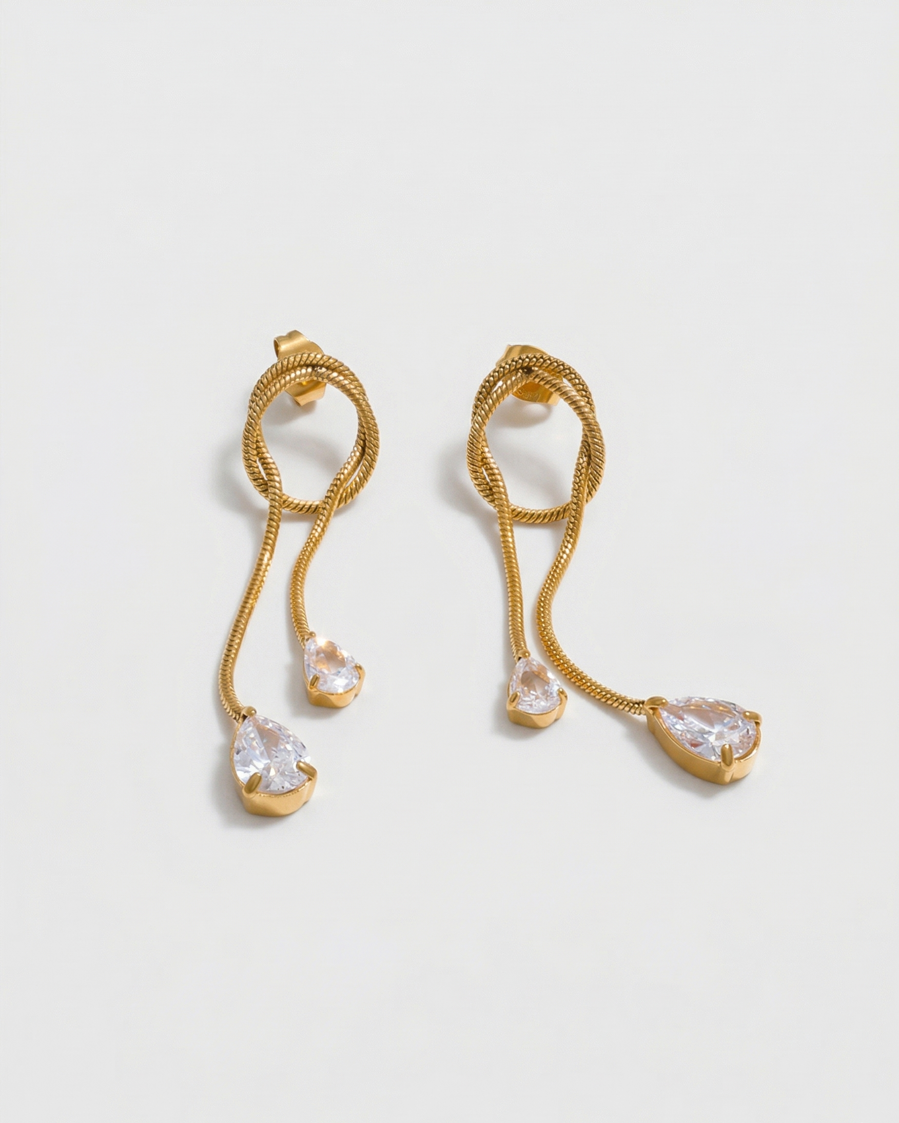 Gold earrings with teardrop-shaped crystals on a light gray background
