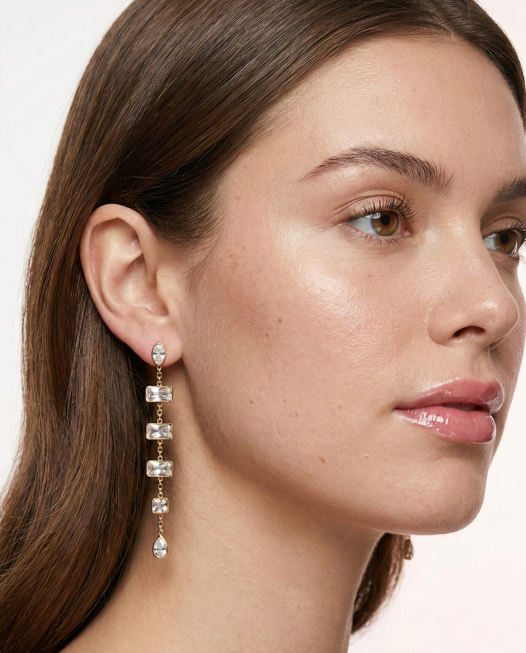Close-up of a woman wearing a dangling earring with a neutral background