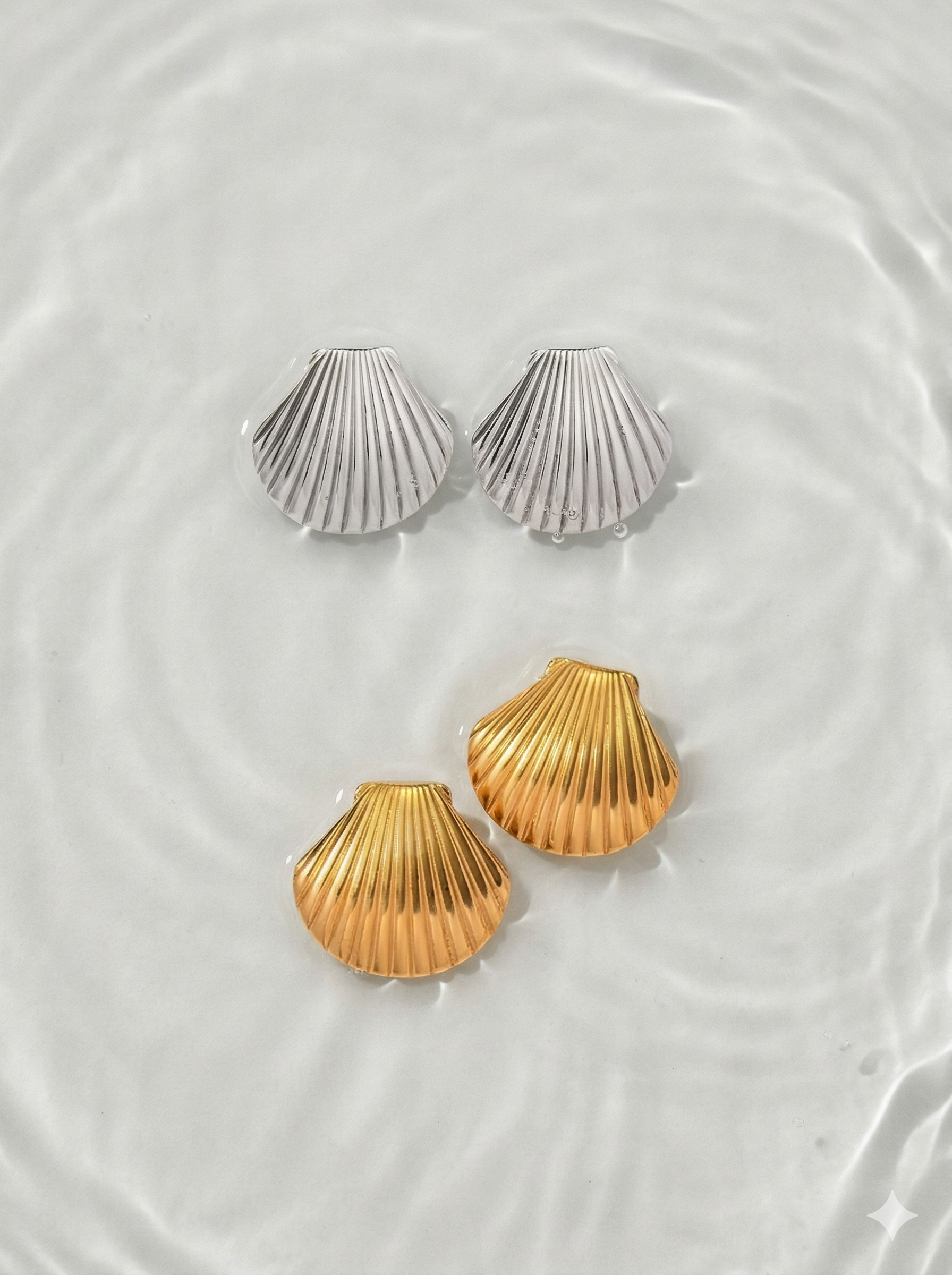Three shell-shaped earrings in gold and silver on a white surface