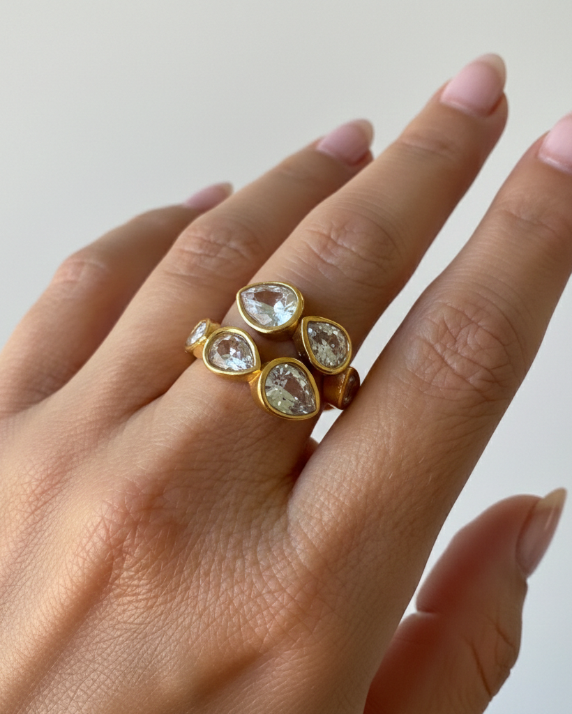 Gold ring with clear gemstones on a hand against a neutral background