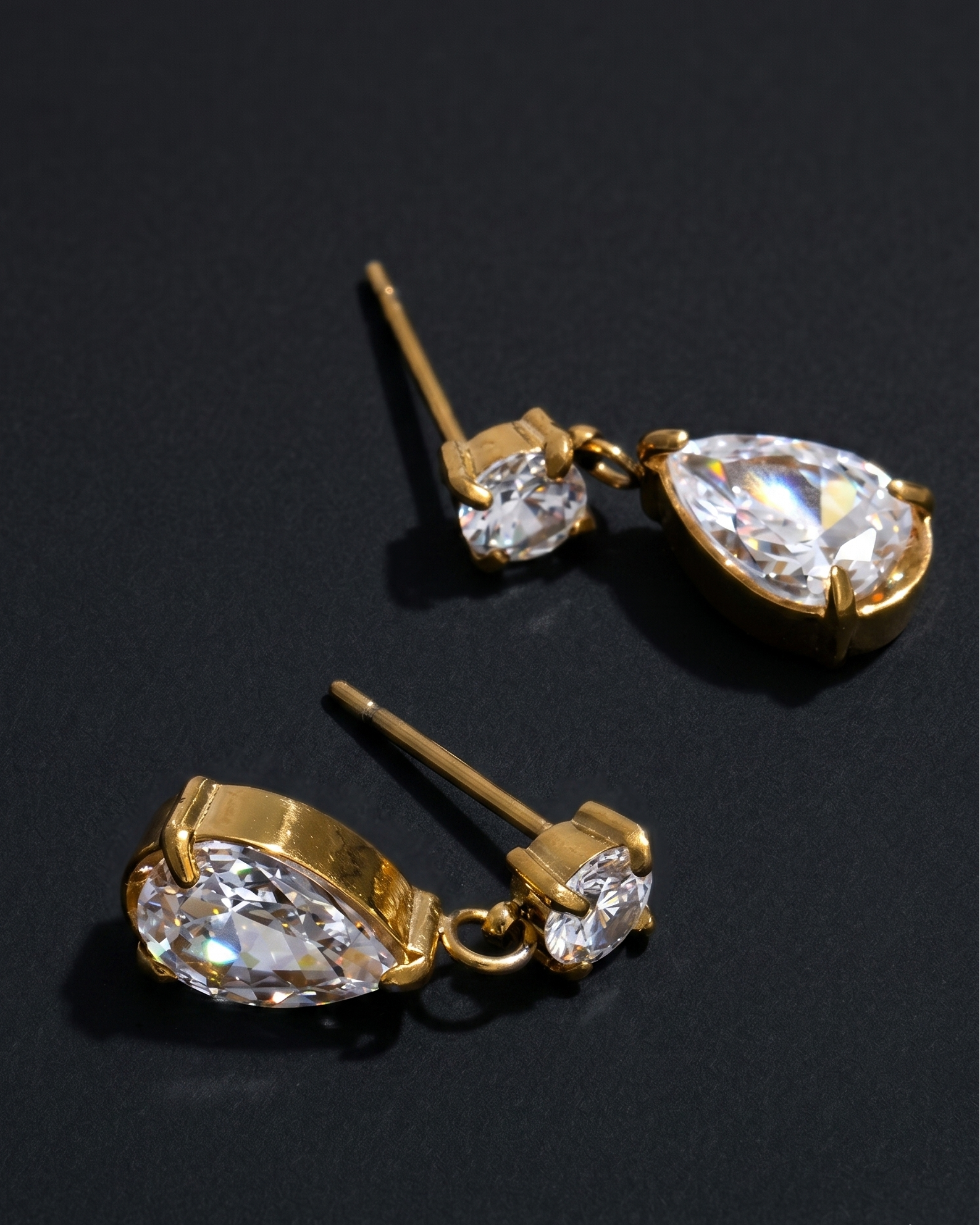 Gold earrings with teardrop-shaped clear gemstones on a black background