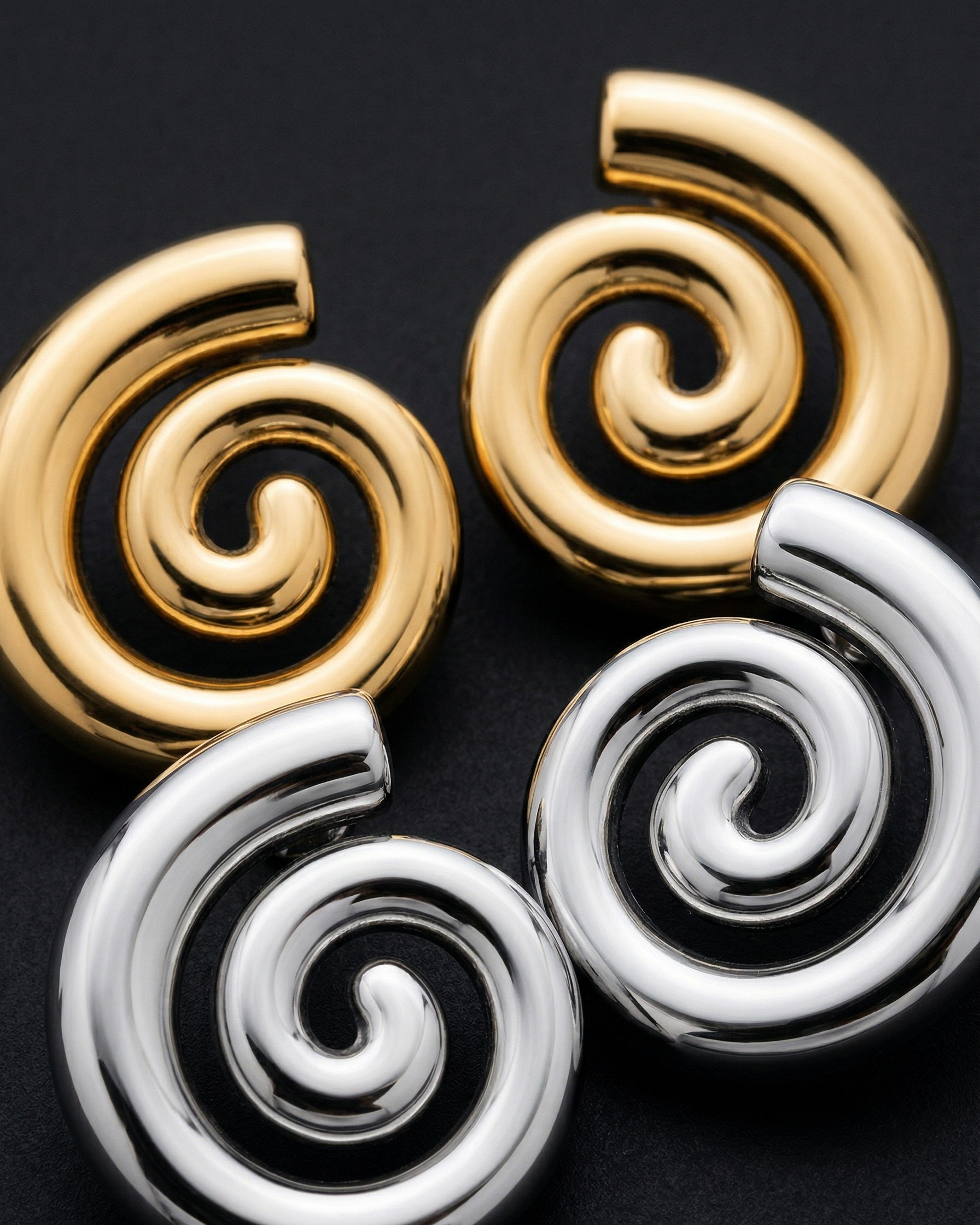 Pair of spiral earrings in gold and silver on a black background
