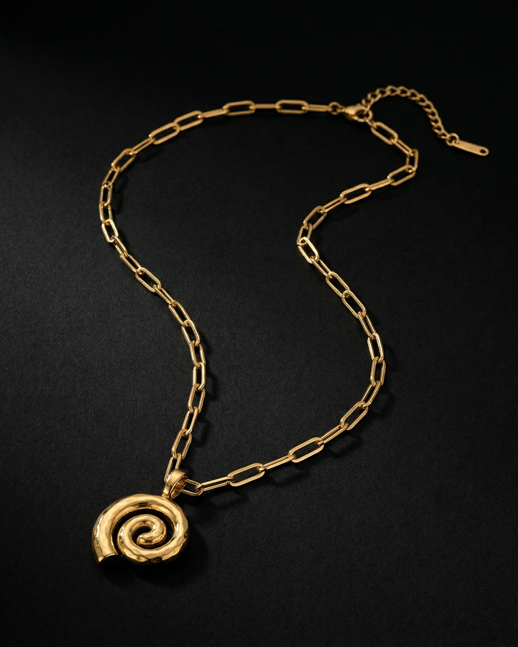 Gold chain necklace with a spiral pendant on a black background