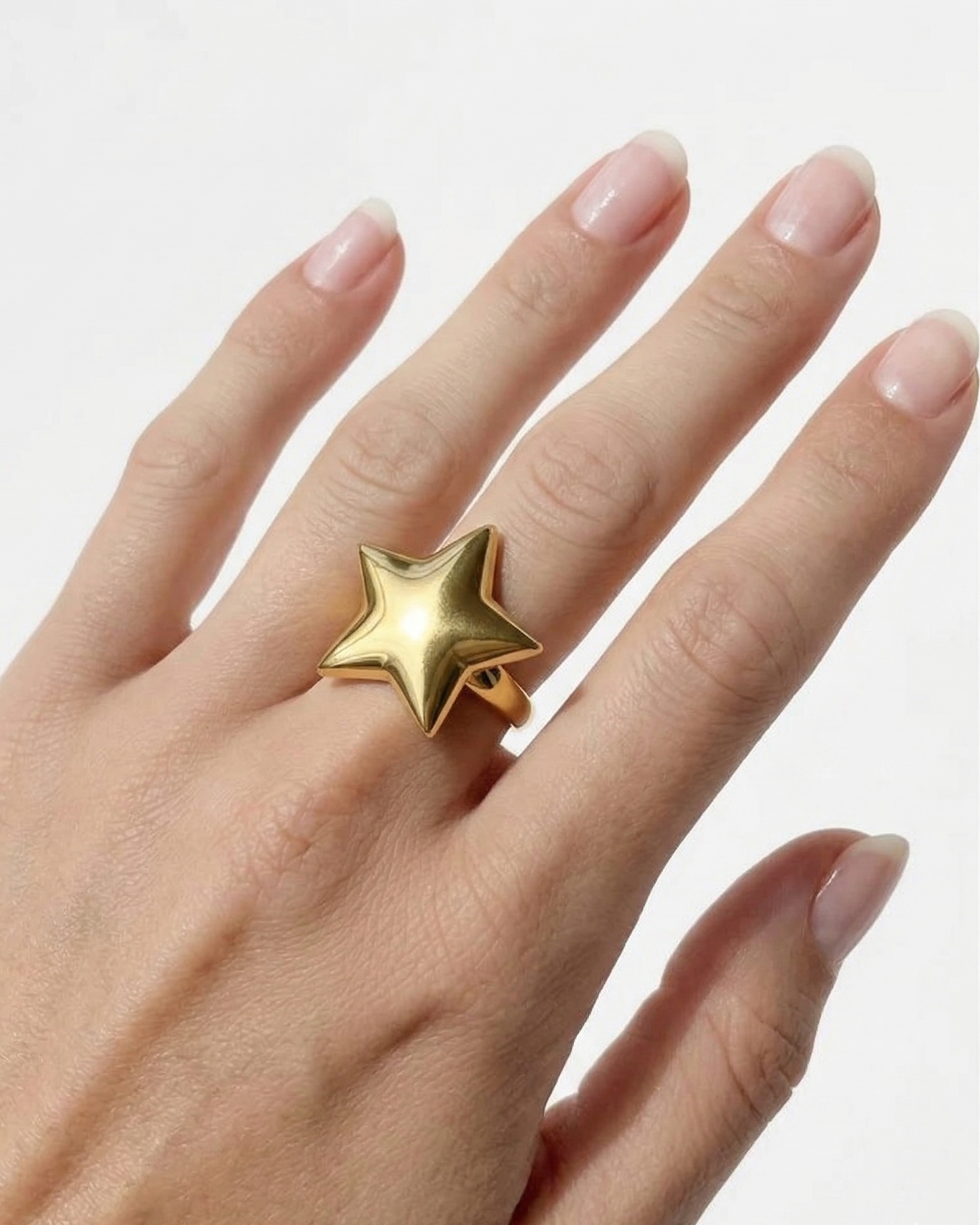 Gold star ring on a hand against a white background