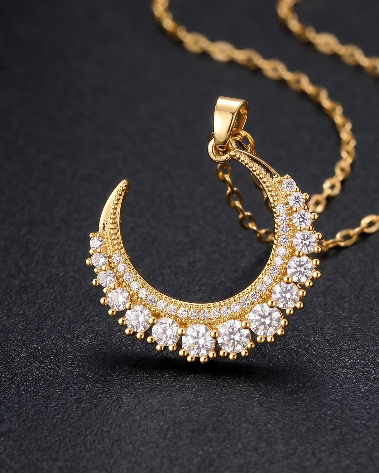 Gold necklace with a crescent moon pendant on a textured beige surface