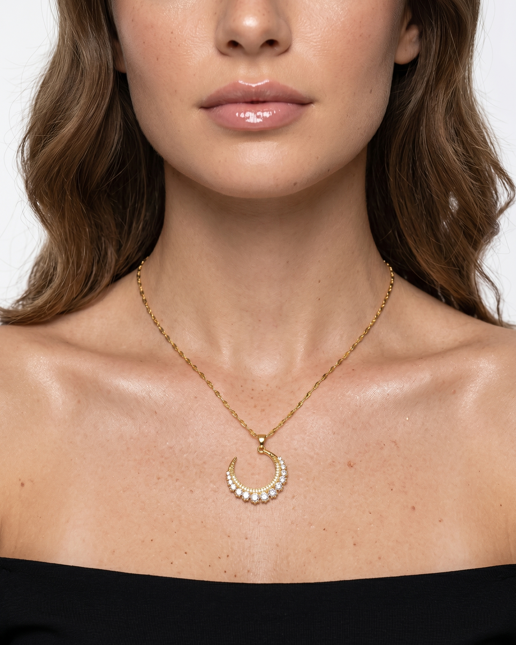 Woman wearing a gold necklace with a crescent moon pendant on a plain background