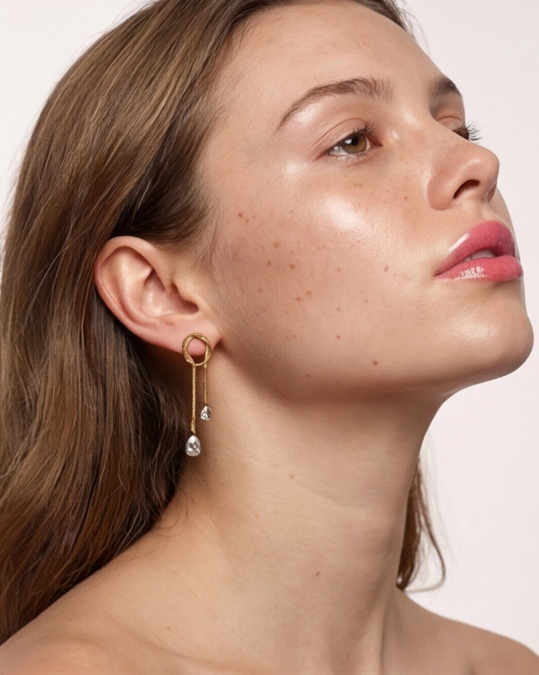 Close-up of a woman wearing a gold earring with a pearl drop on a plain background
