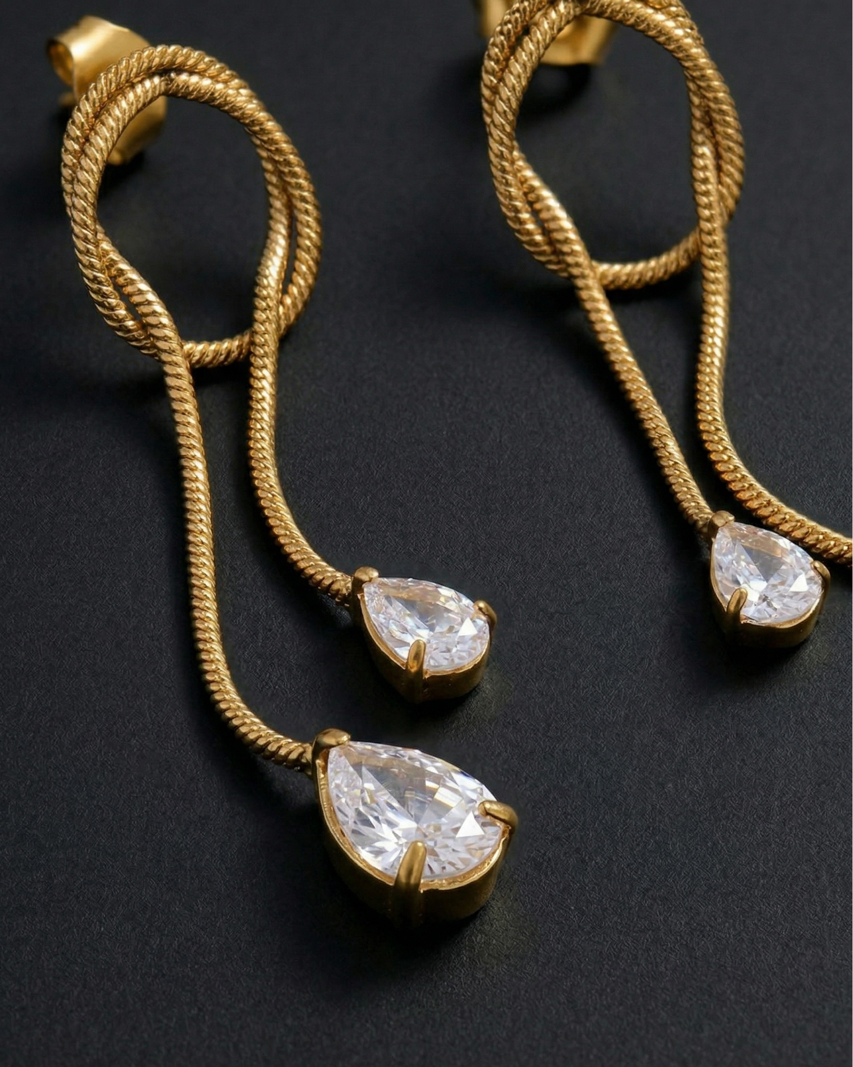 Gold earrings with teardrop-shaped gemstones on a dark background