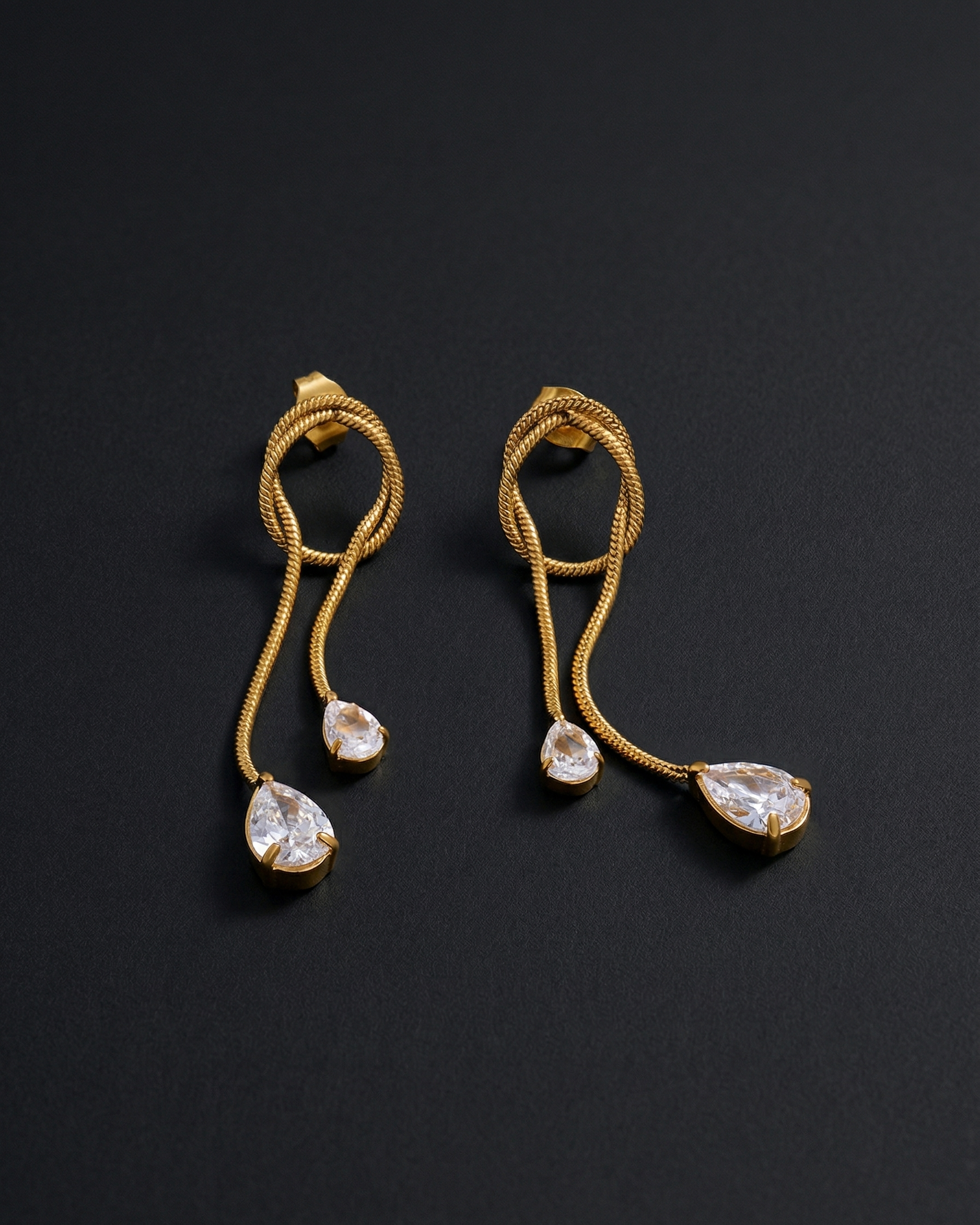 Gold earrings with teardrop-shaped gemstones on a dark background