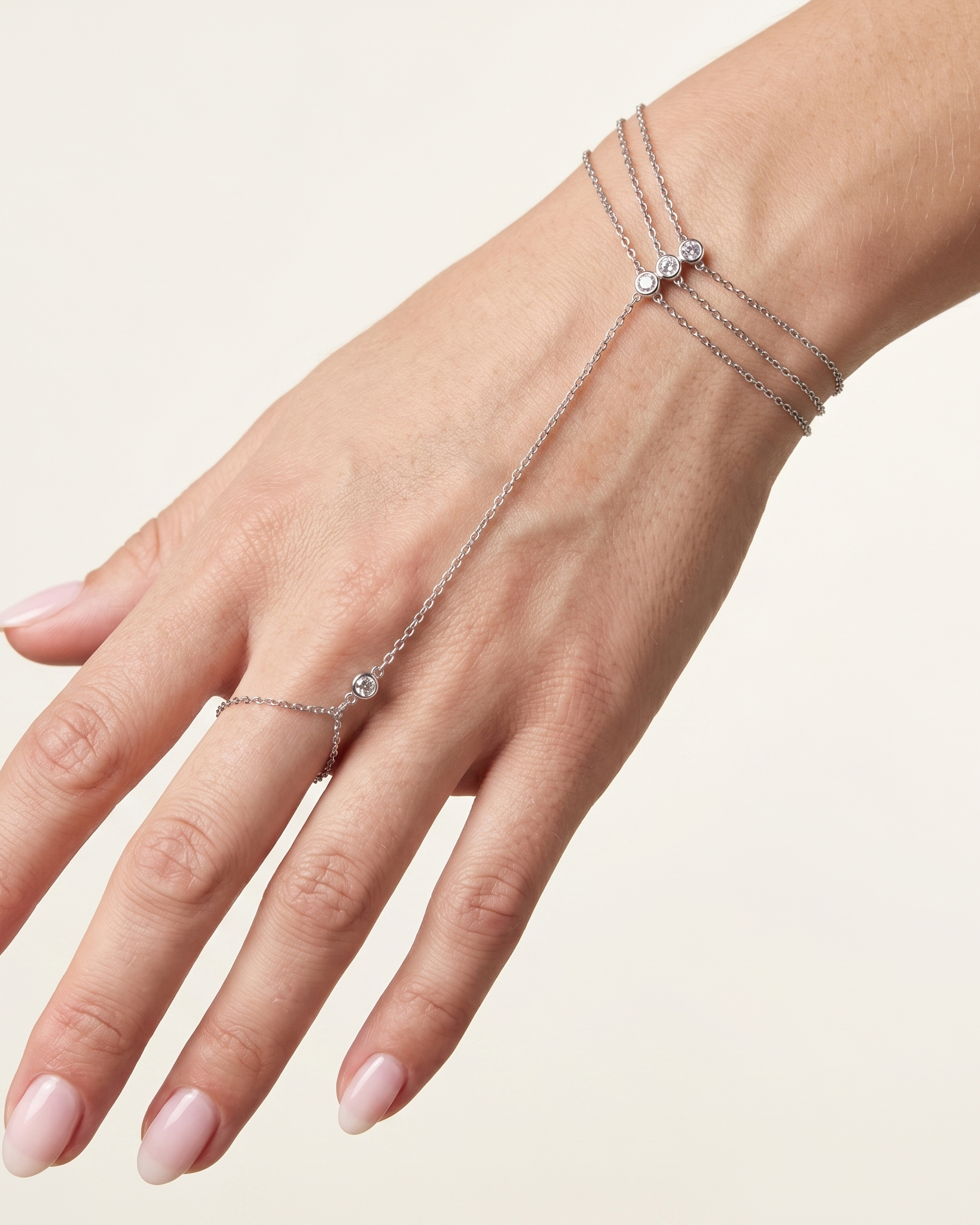 Hand wearing a delicate silver bracelet on a plain background