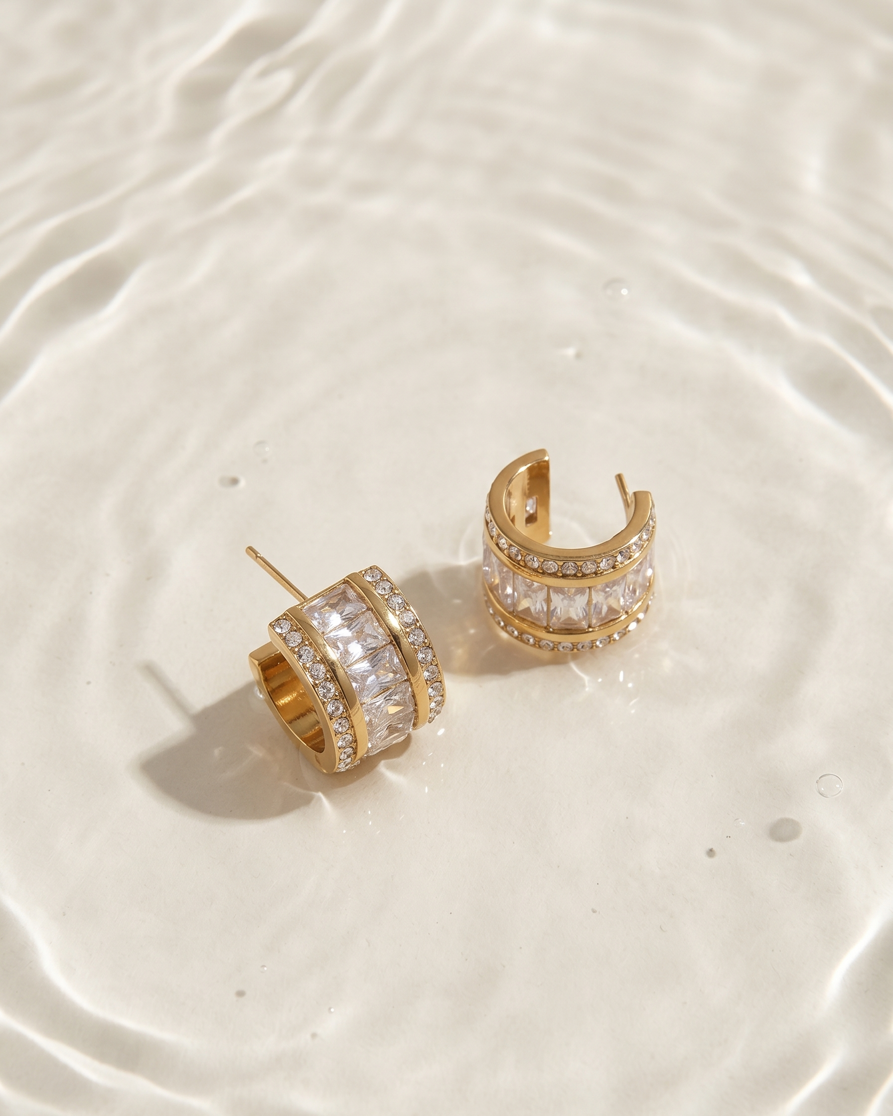 Gold hoop earrings with clear stones on a beige surface