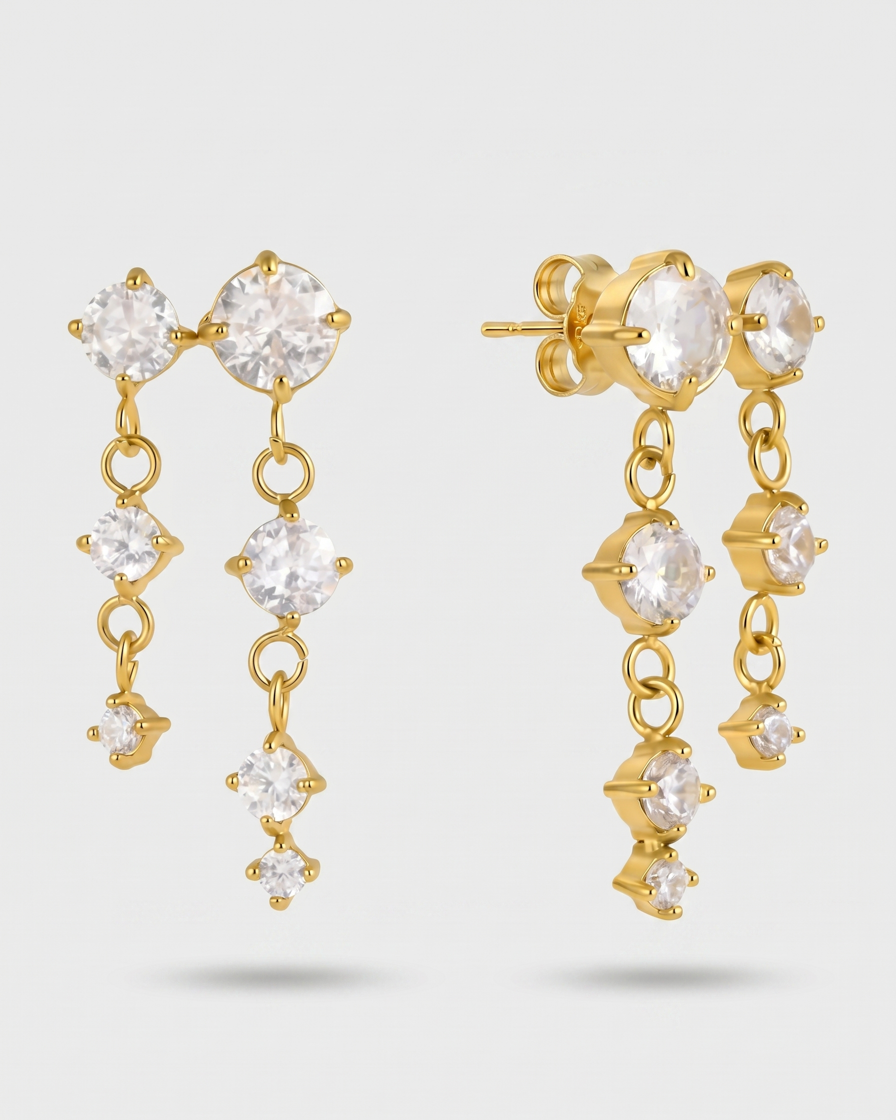 Gold earrings with clear gemstones on a light gray background