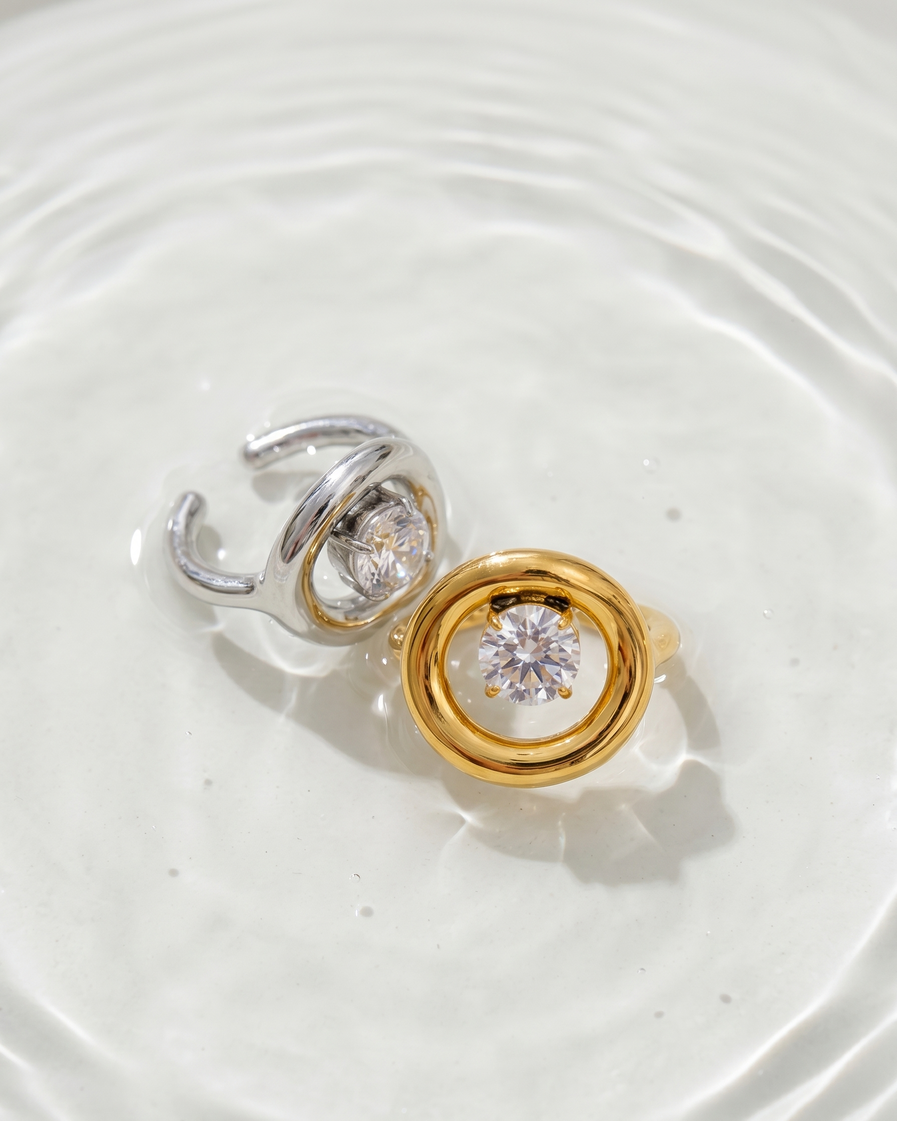 Gold and silver earrings with clear gemstones on a white surface