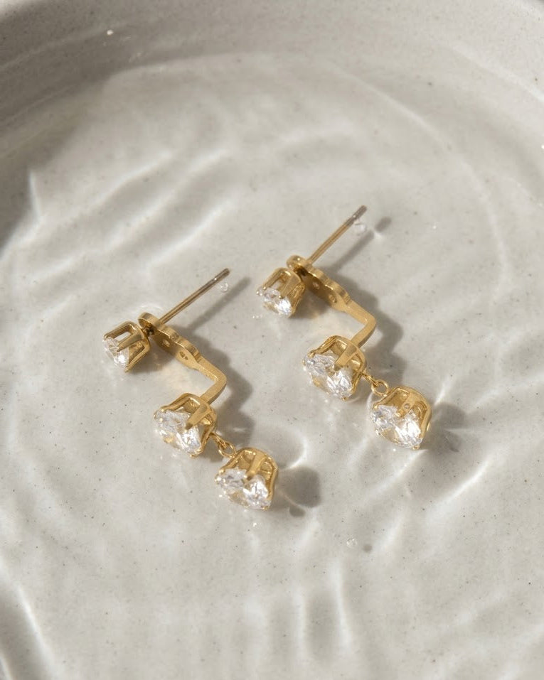 Gold earrings with clear stones on a light gray surface