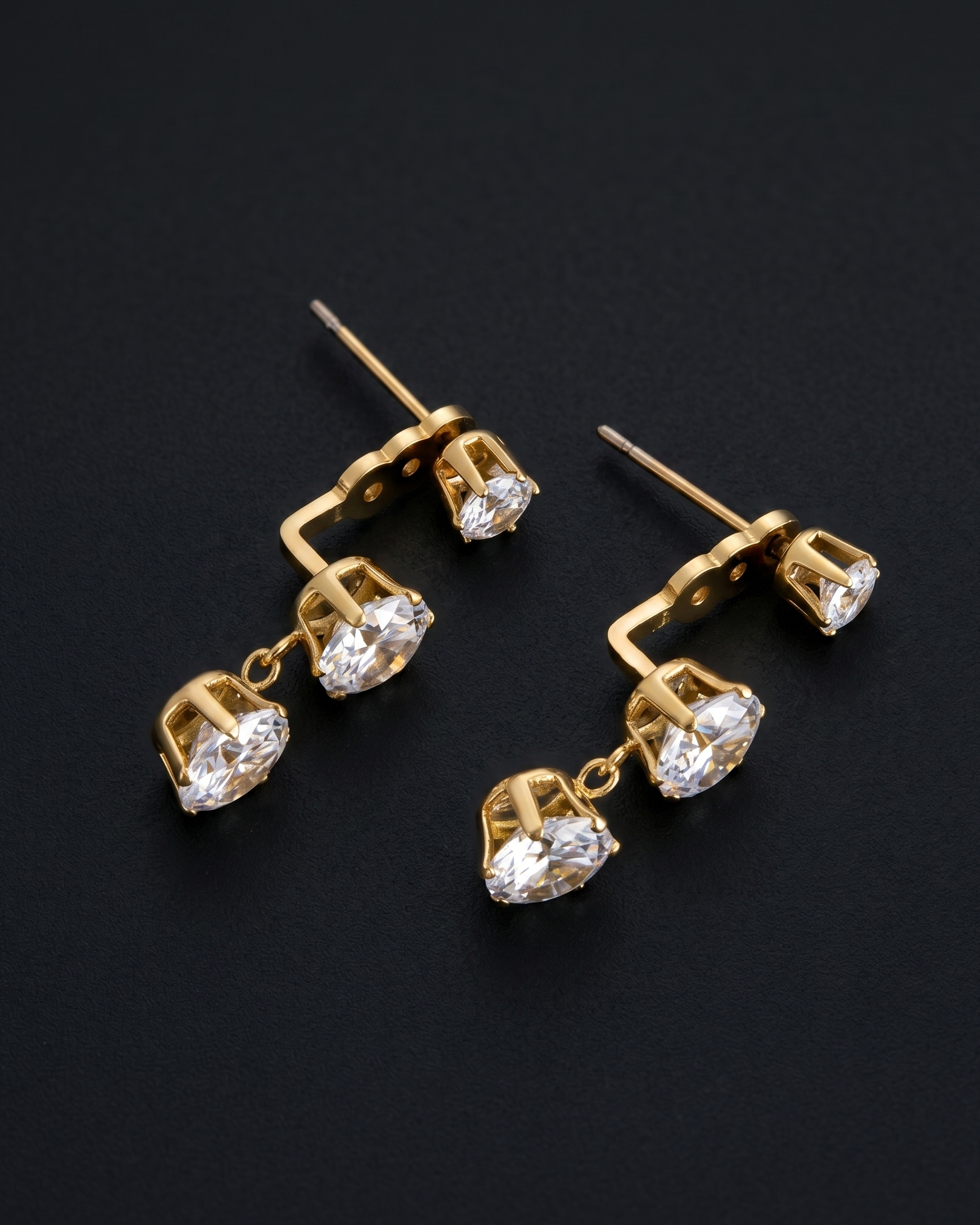Pair of gold earrings with clear gemstones on a black background