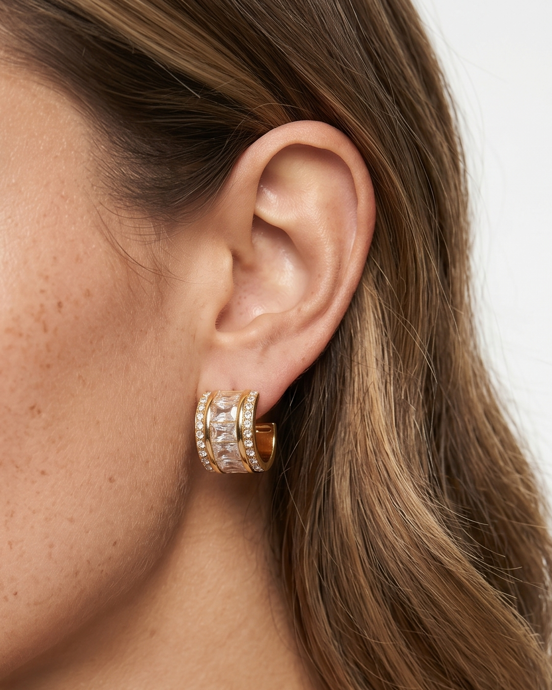 Close-up of a woman wearing gold hoop earrings with a neutral background