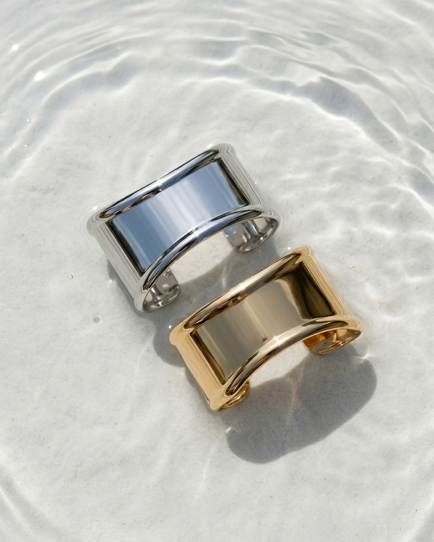 Two metallic rings, one silver and one gold, on a reflective water surface.