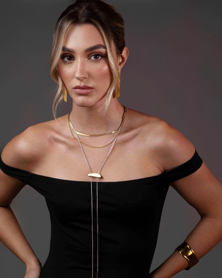 Woman wearing a black off-shoulder dress with gold jewelry against a dark background