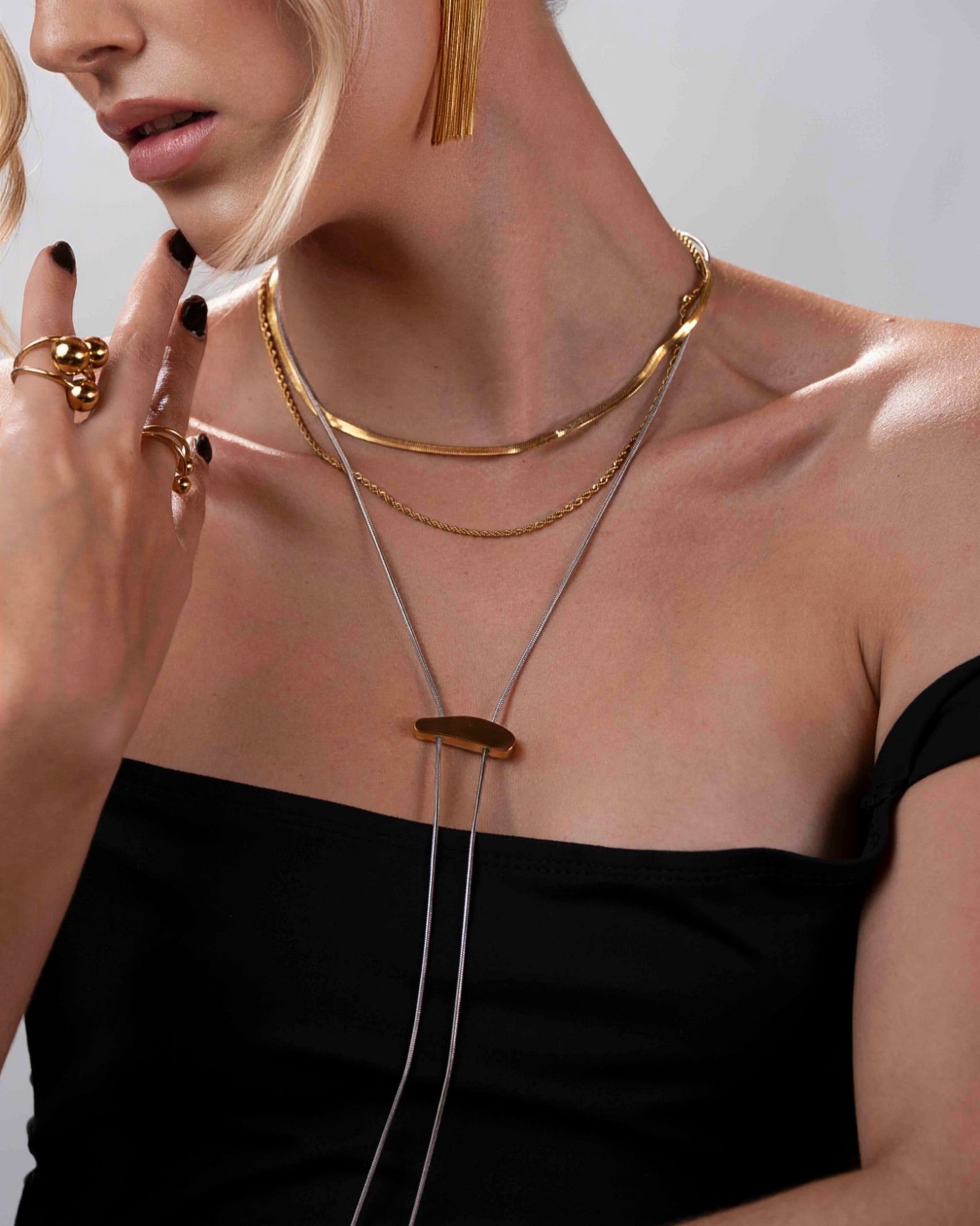 Woman wearing gold necklaces and rings on a plain background