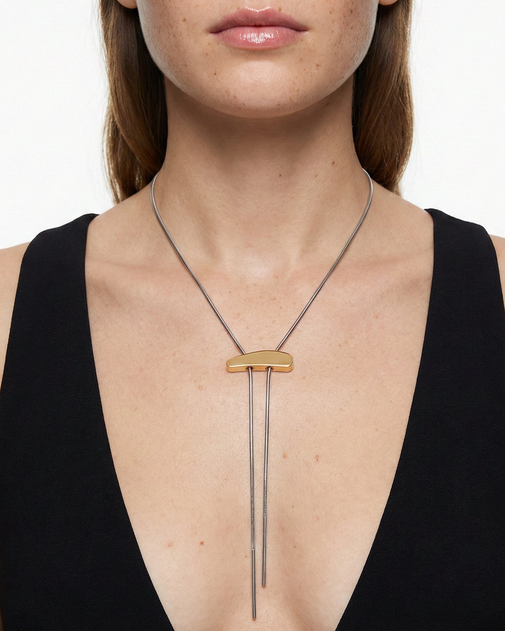 Necklace with a gold bar and dangling elements worn by a model on a white background