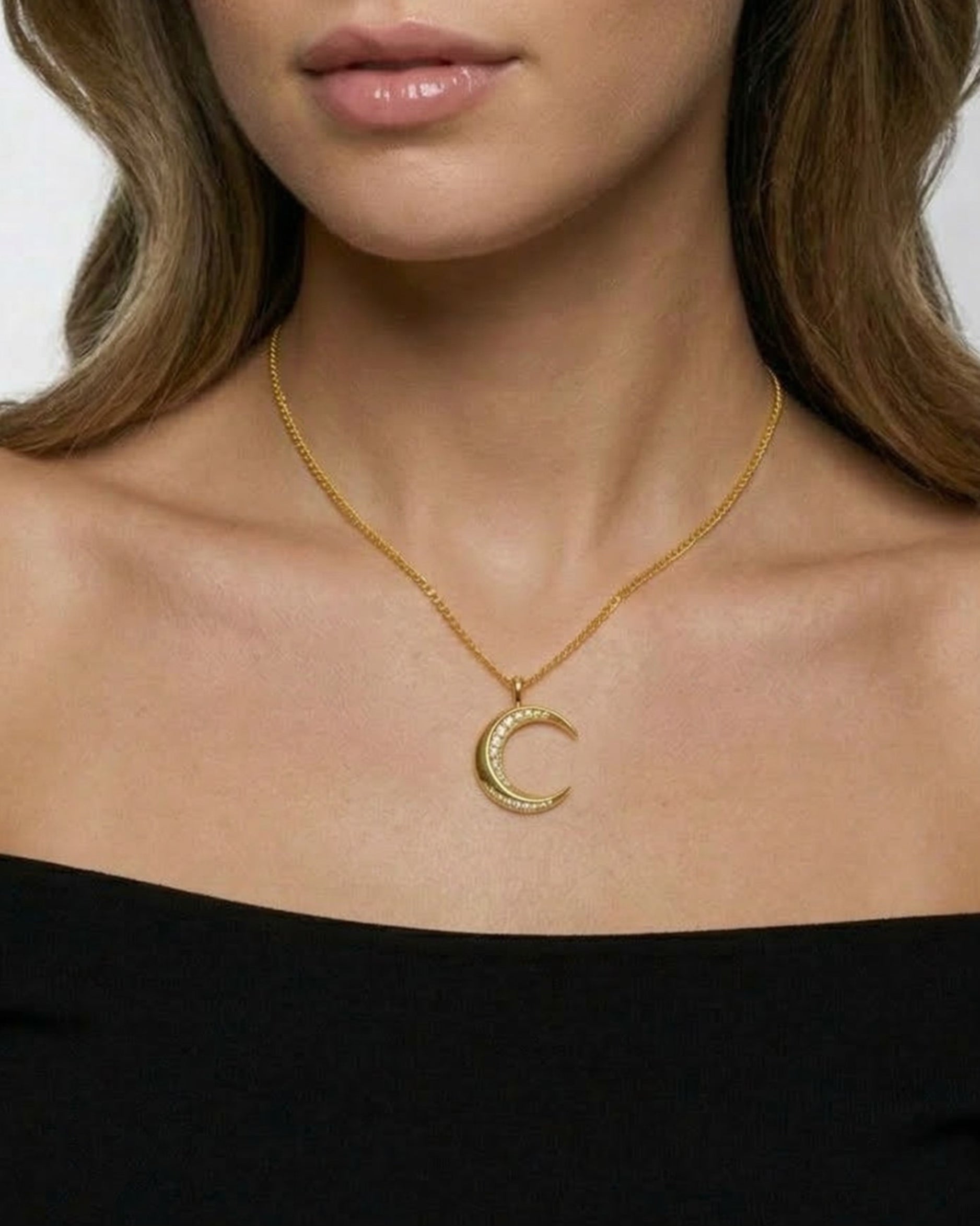 Gold necklace with a crescent moon pendant worn by a model against a neutral background