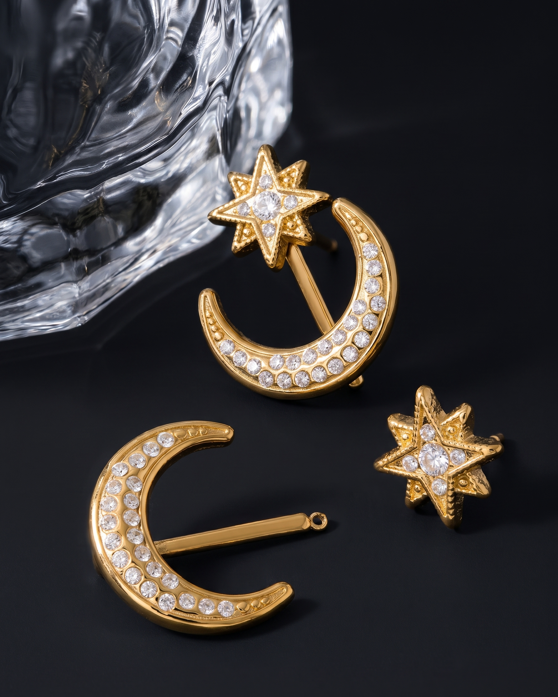 Gold earrings with star and crescent moon designs on a dark background