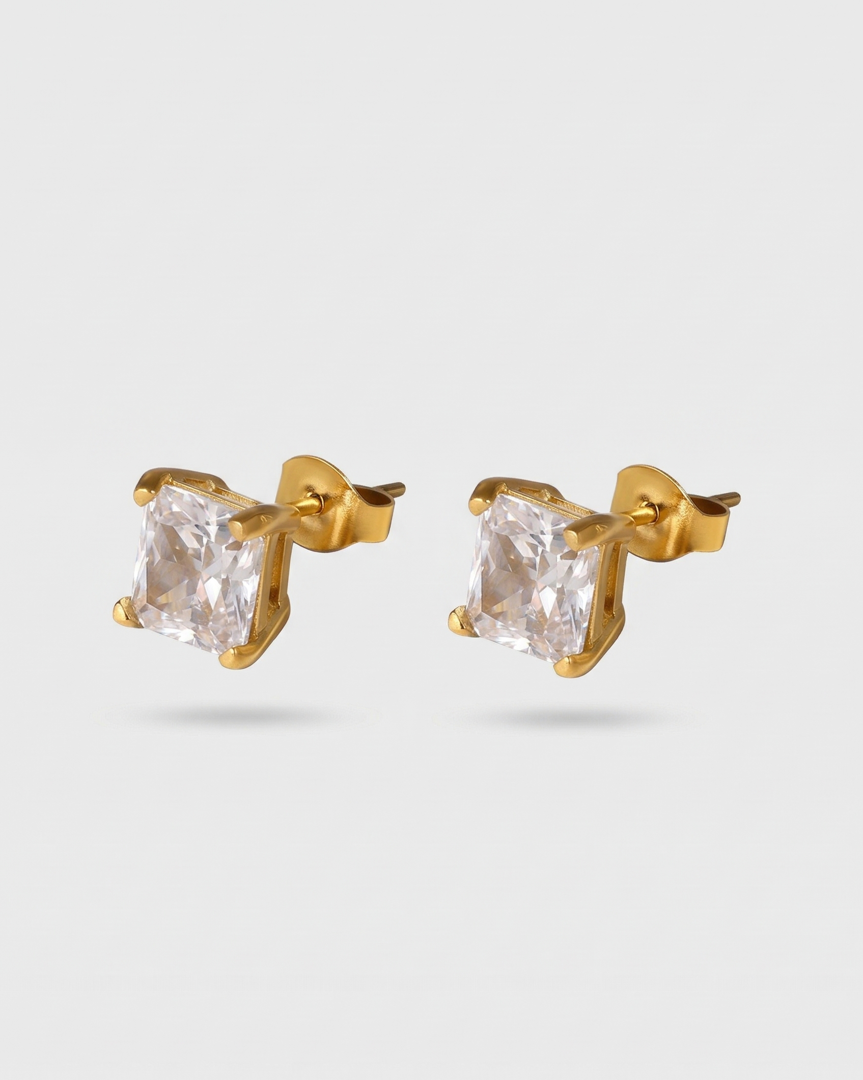 Gold stud earrings with clear gemstones on a light gray background