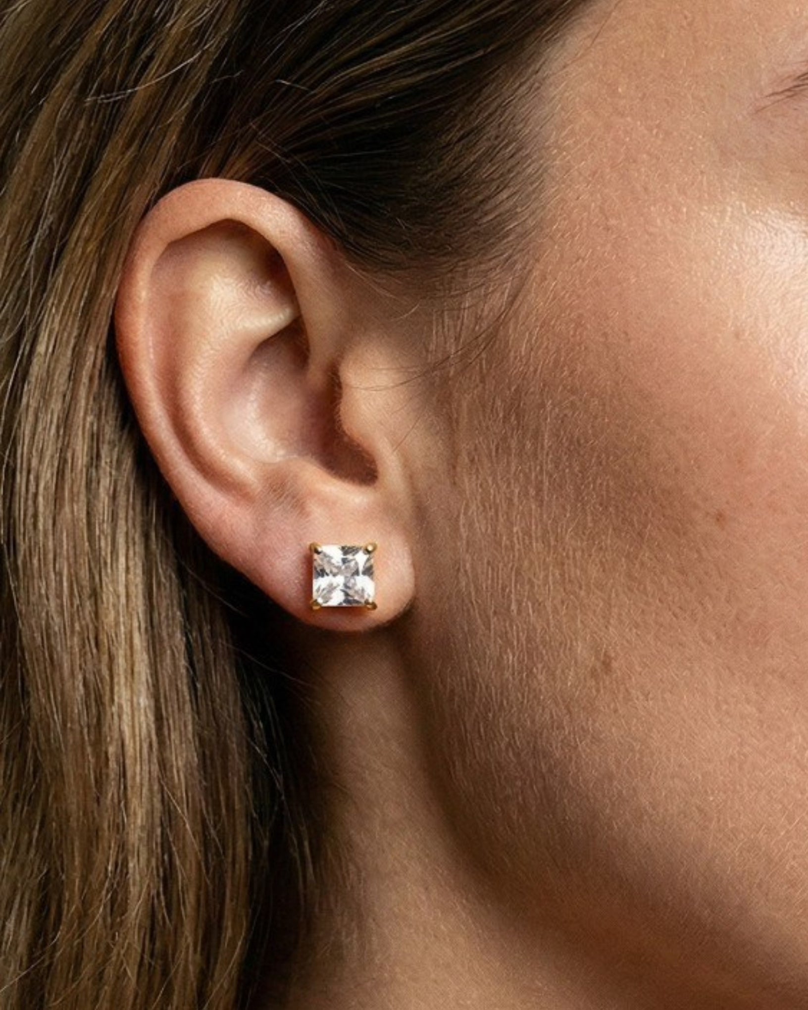 Close-up of an ear wearing a square stud earring with a diamond.