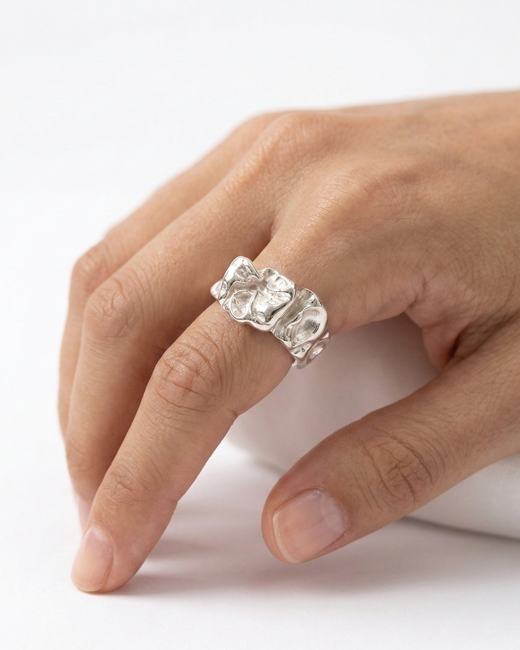 Hand wearing a silver ring with a large gemstone on a white background