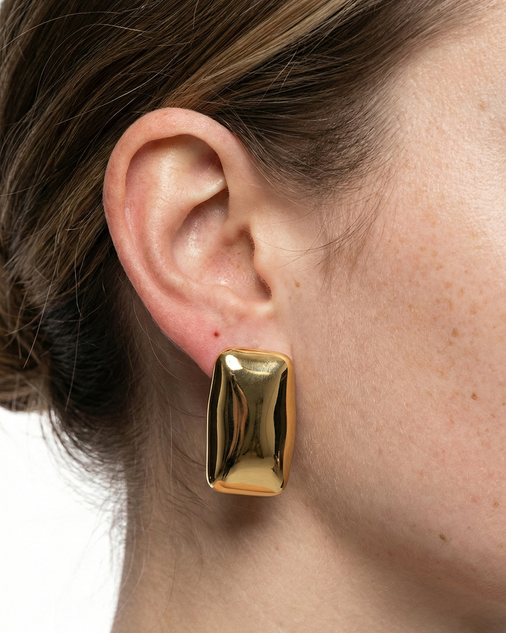 Gold earring worn by a person with a neutral background