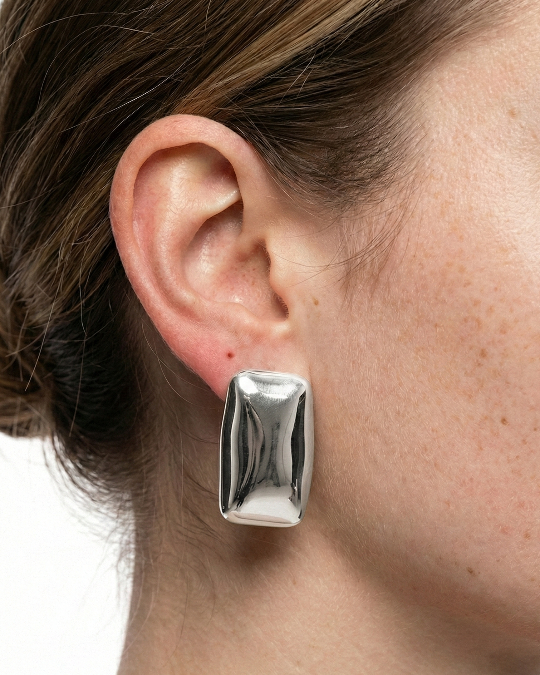 Silver earring worn by a person with a neutral background
