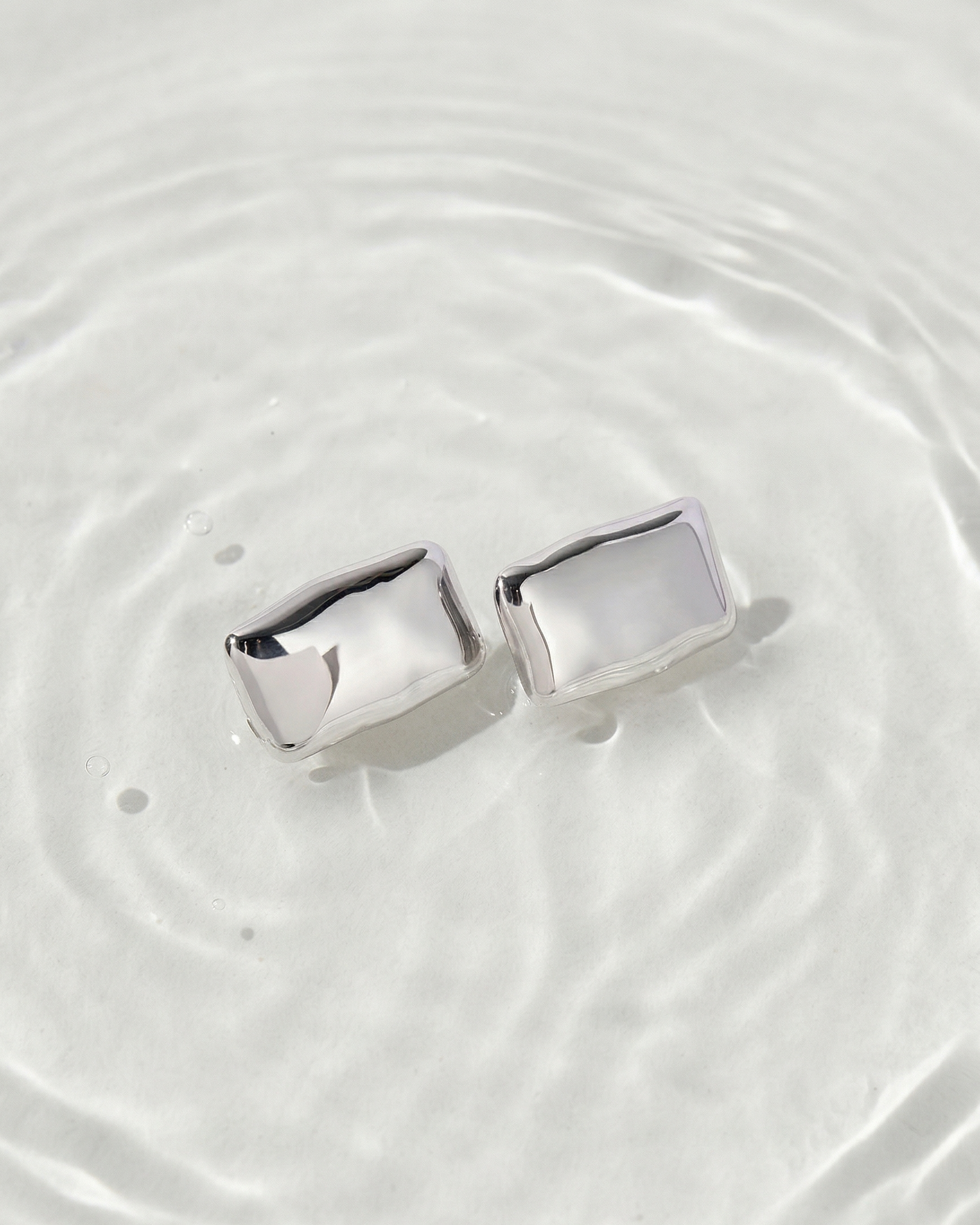 Silver earrings on a white surface with water droplets