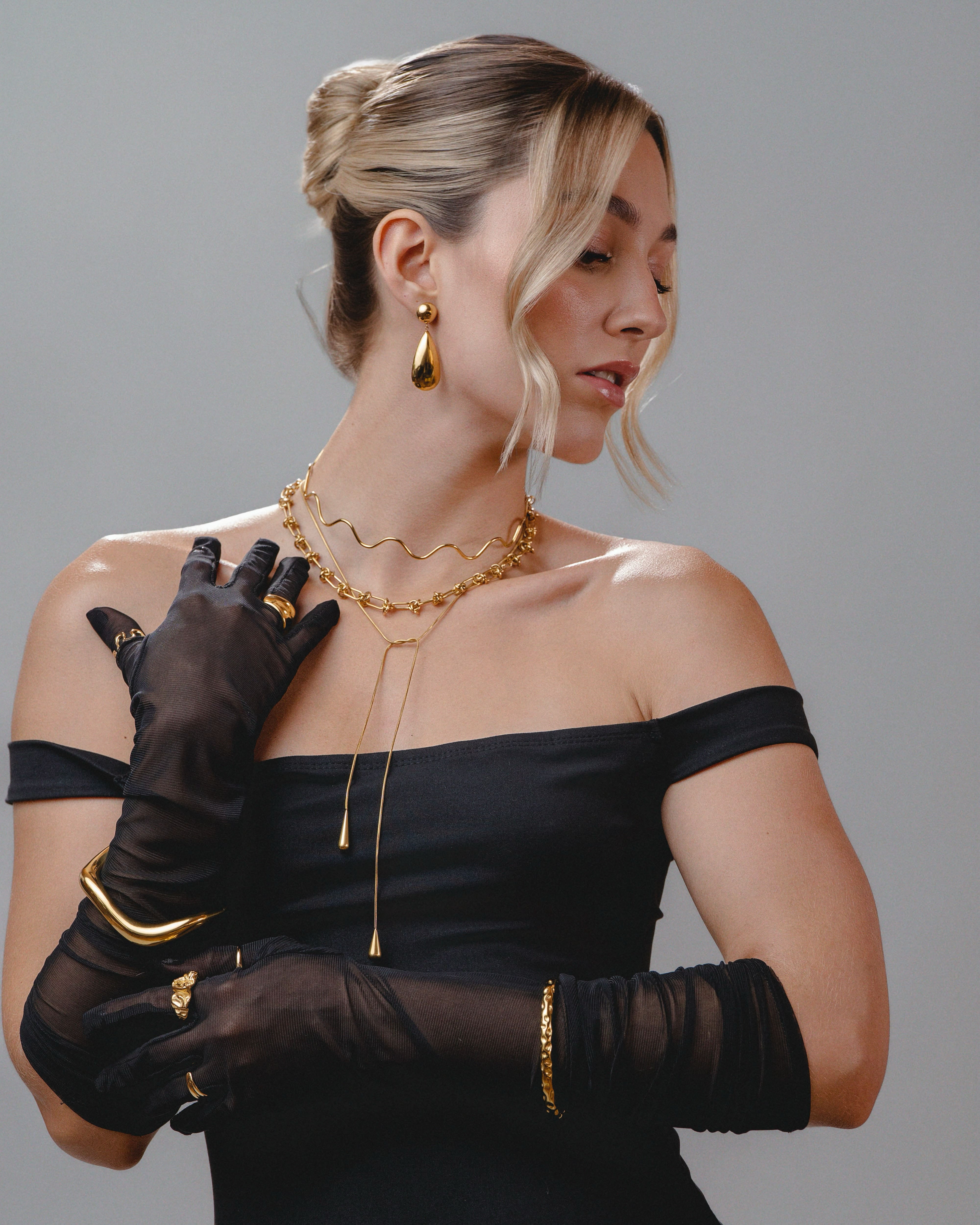 Woman wearing black gloves and gold jewelry against a gray background