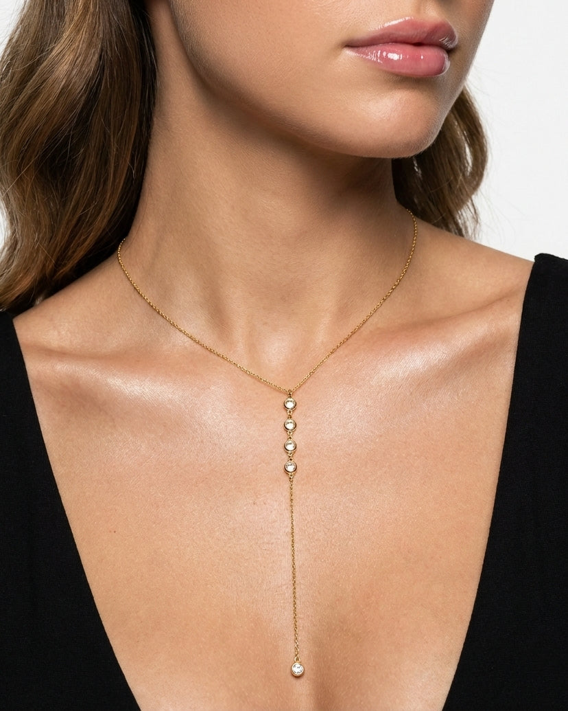 Gold necklace with dangling beads worn by a model against a neutral background