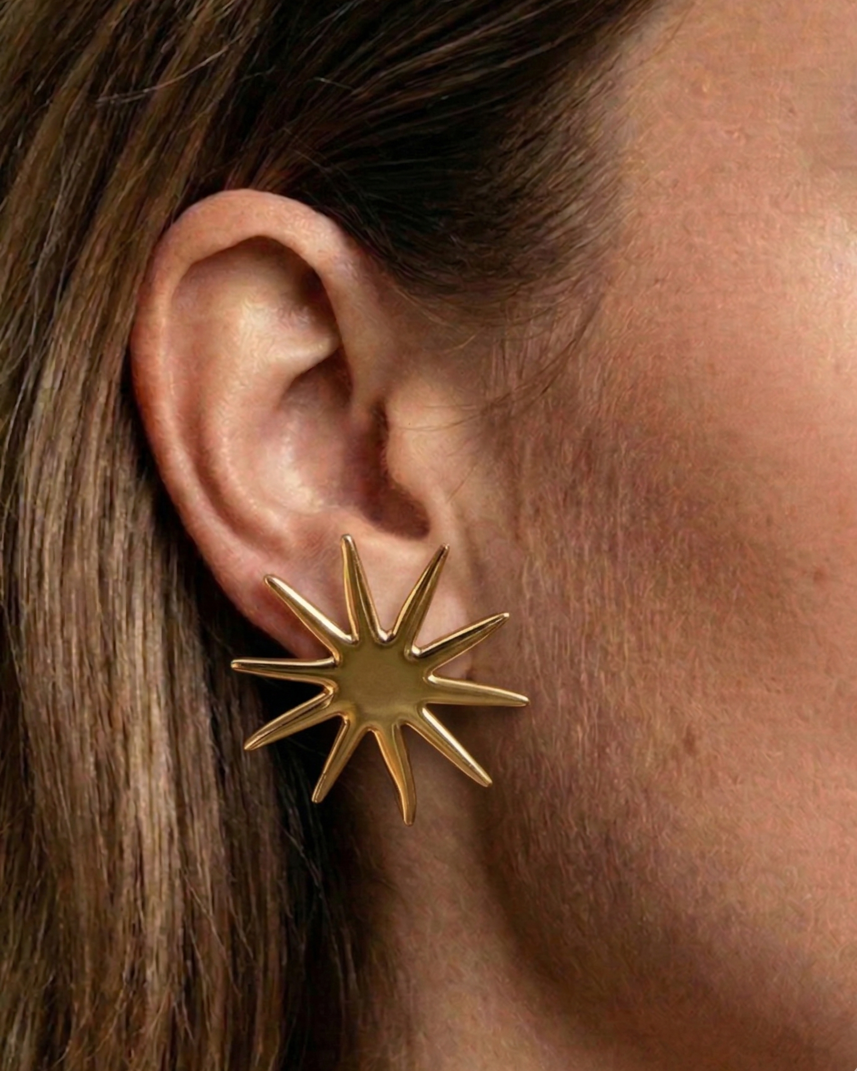 Gold star-shaped earring worn by a person