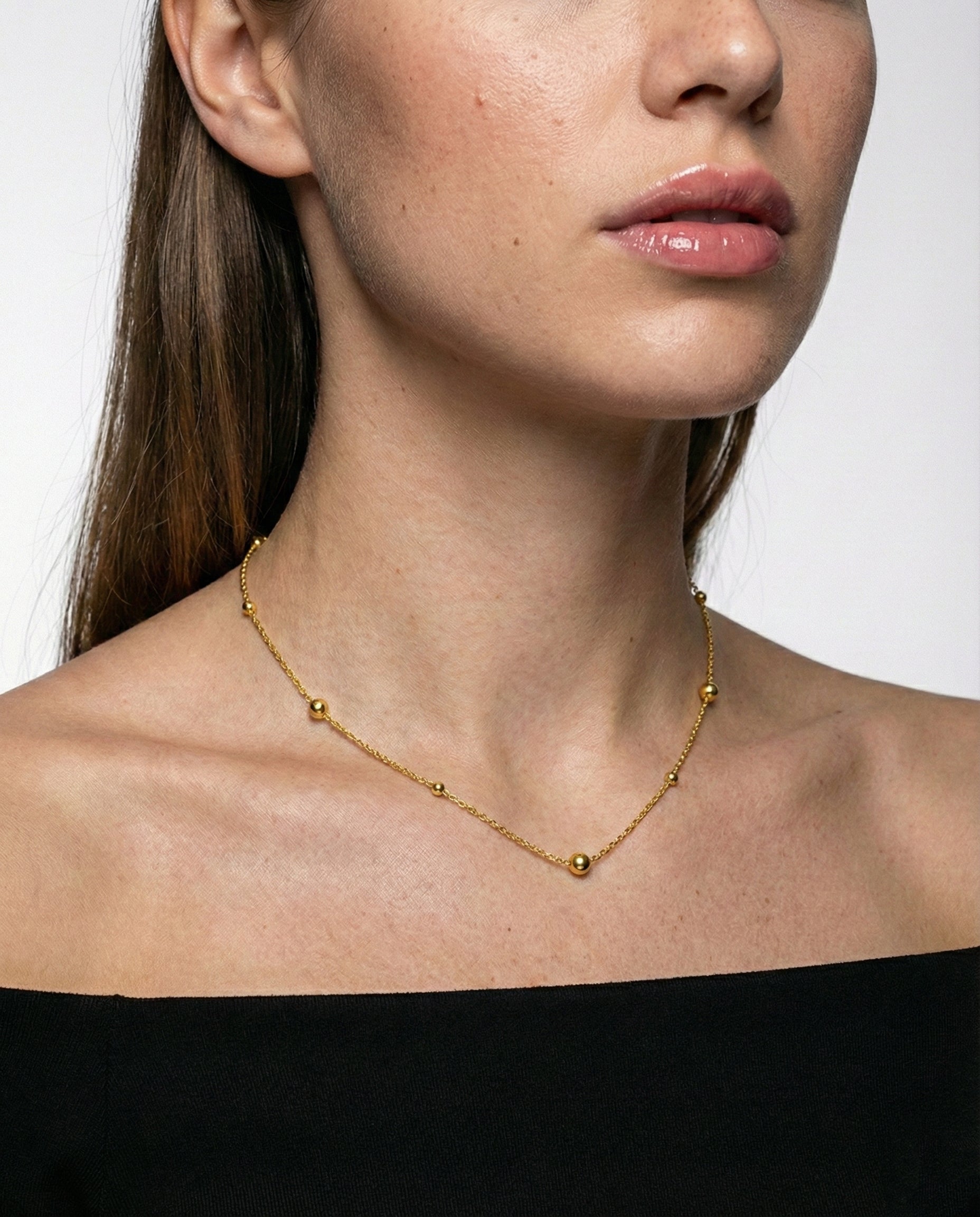 Close-up of a person wearing a gold necklace against a neutral background