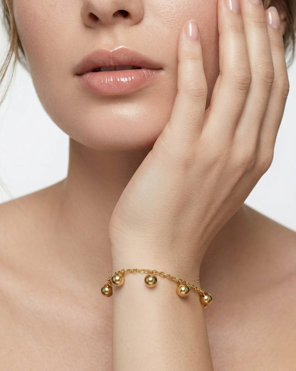 Close-up of a woman's face with a gold bracelet on her wrist against a neutral background