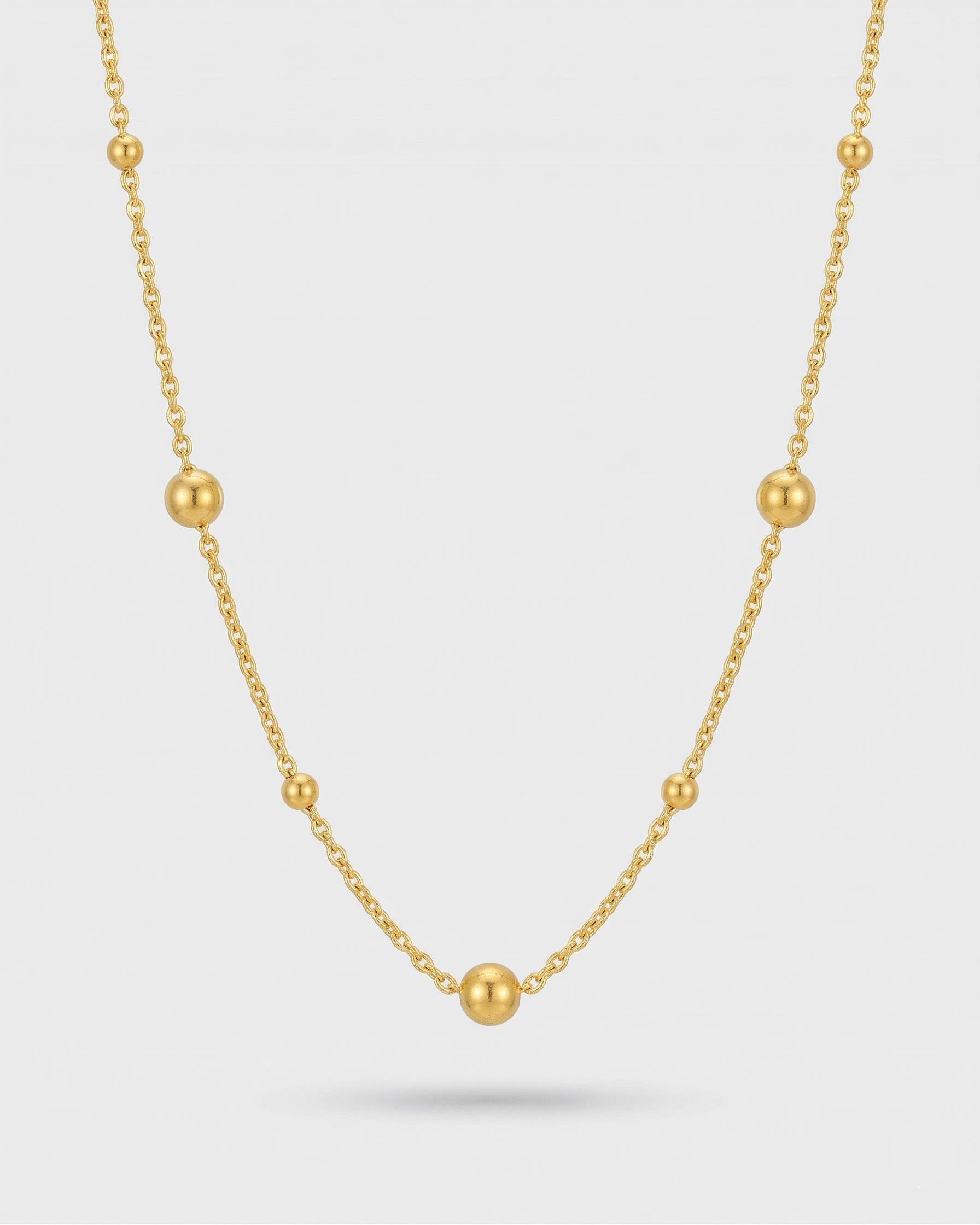 Gold necklace with small beads on a light gray background