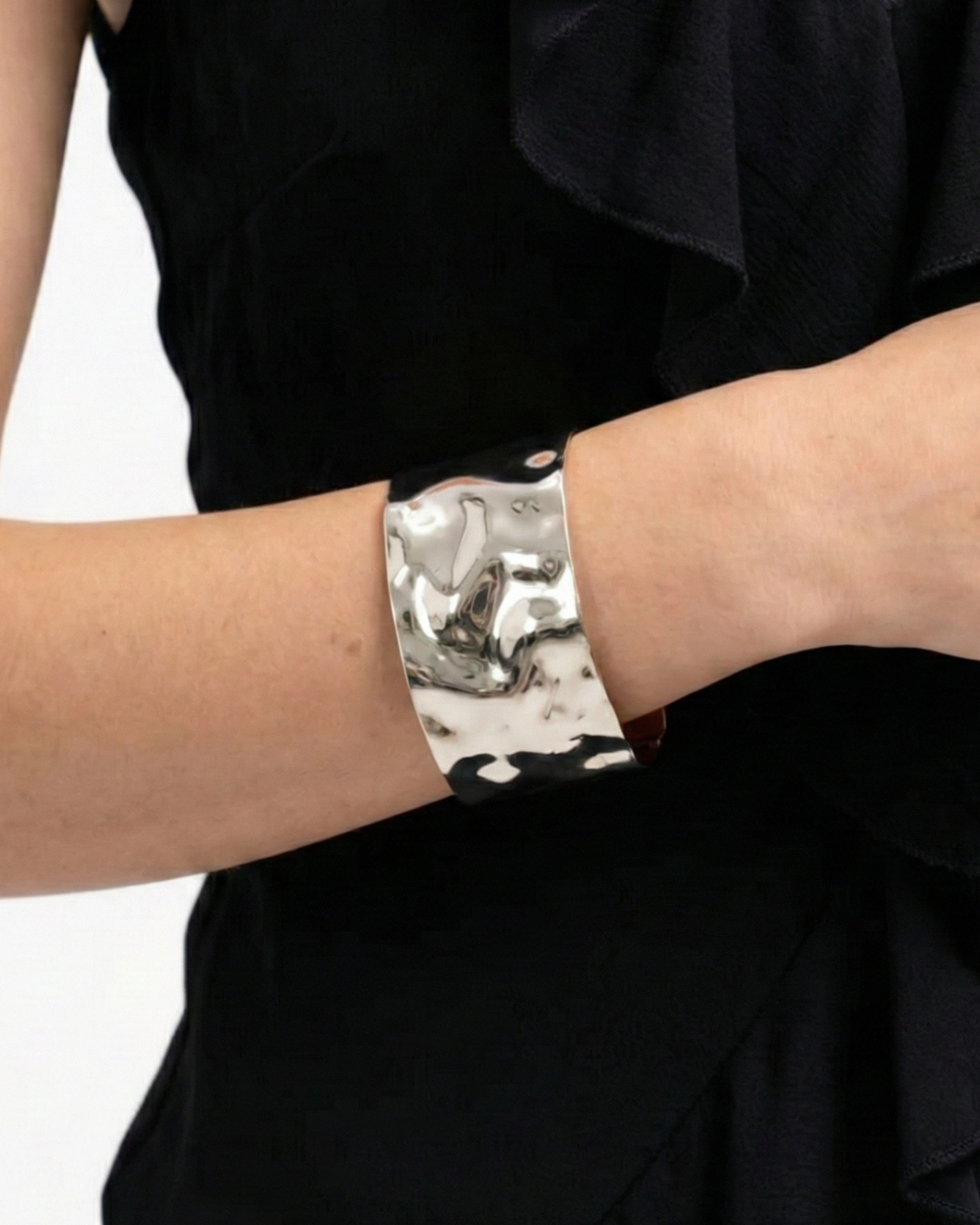 Silver cuff bracelet on a person wearing a black dress against a white background