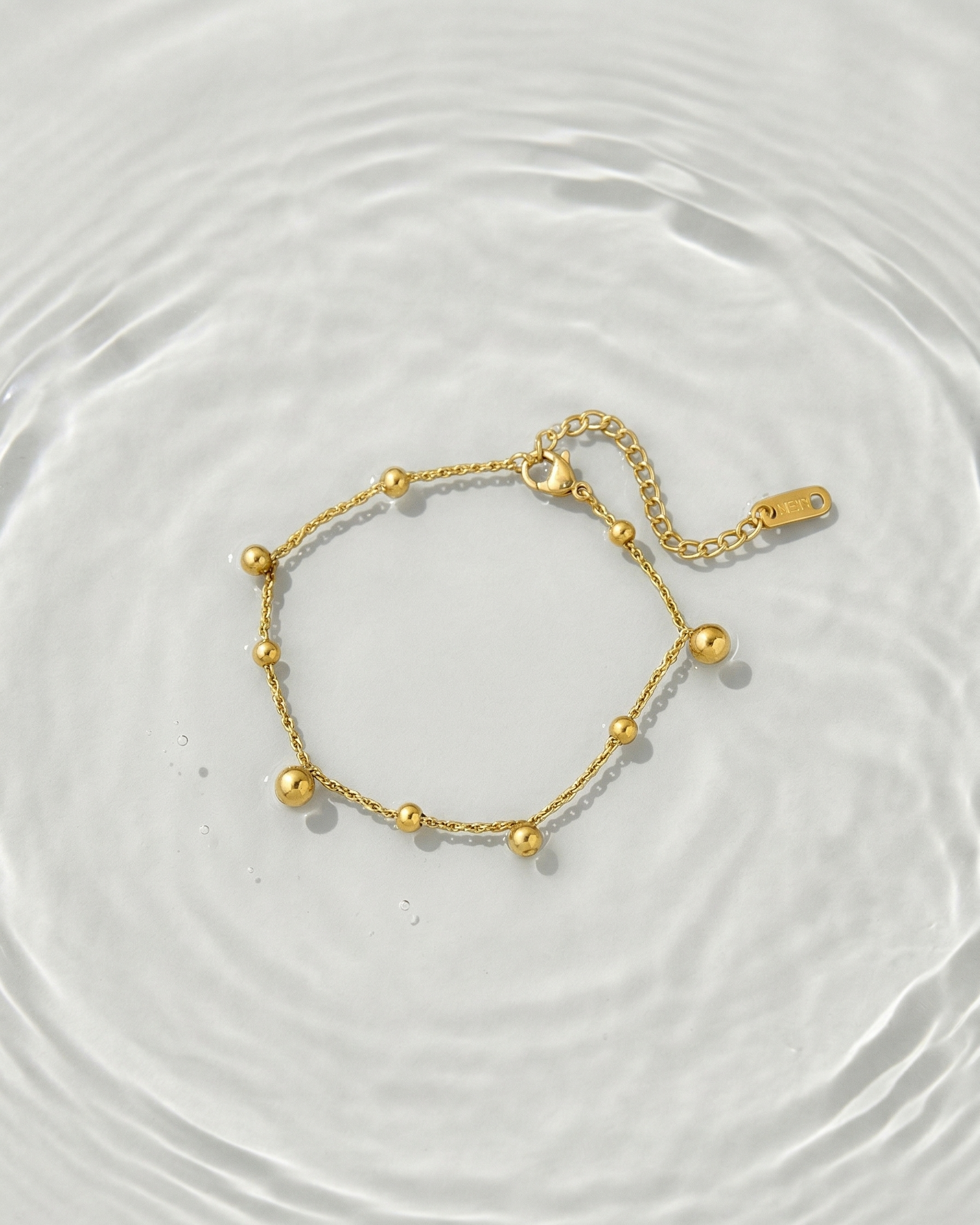 Gold bracelet on a white surface with water ripples