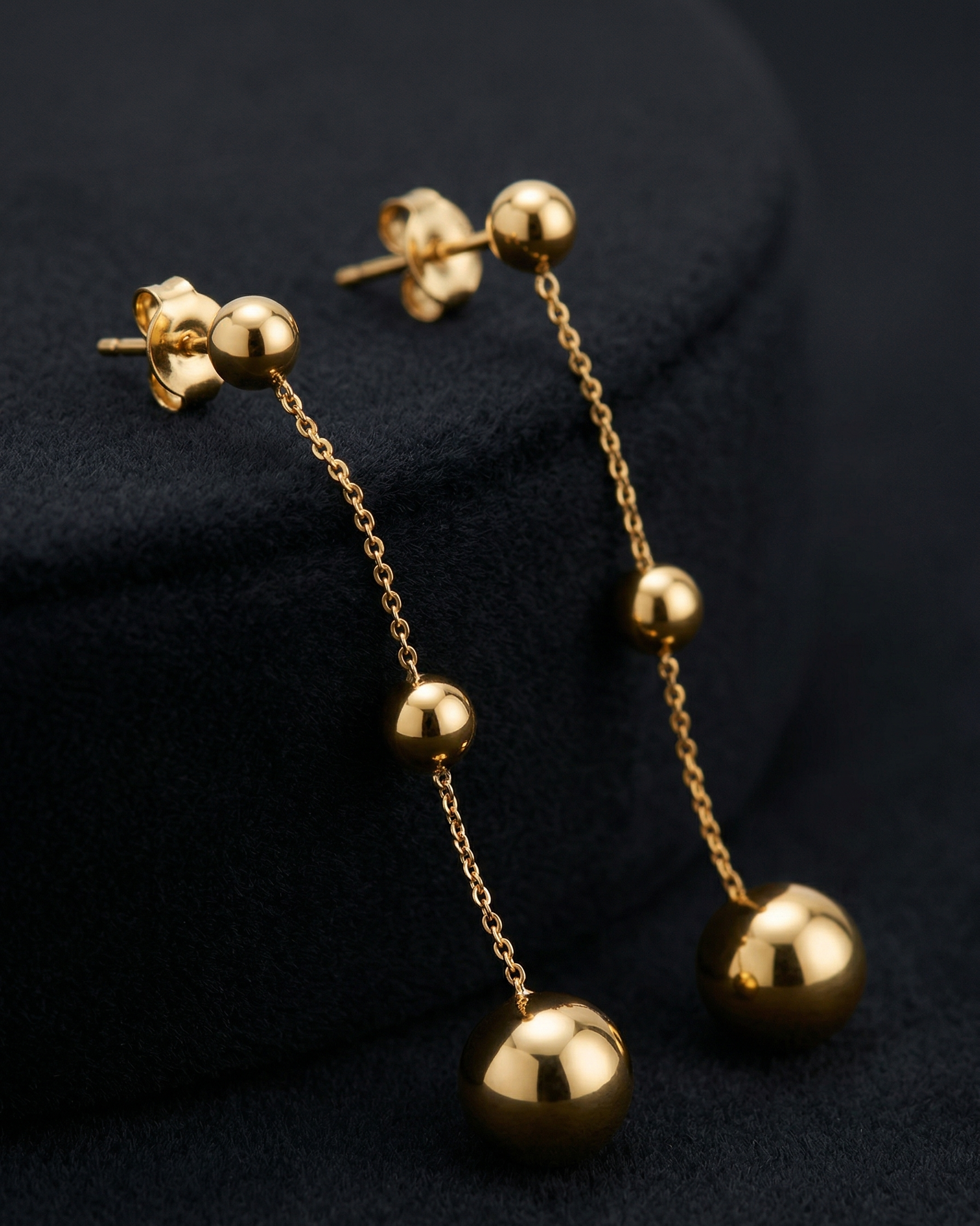 Gold chain earrings with spherical ends on a dark background