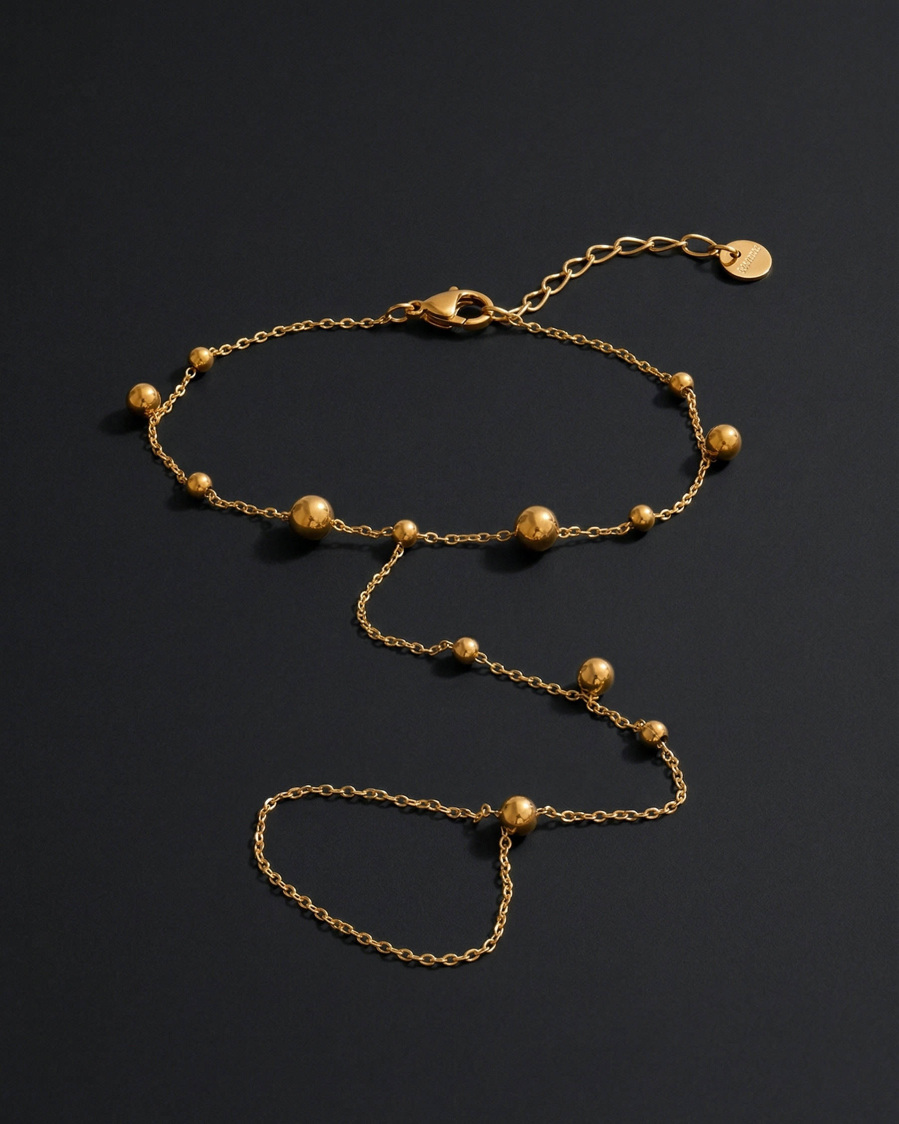 Gold anklet with small beads on a dark background