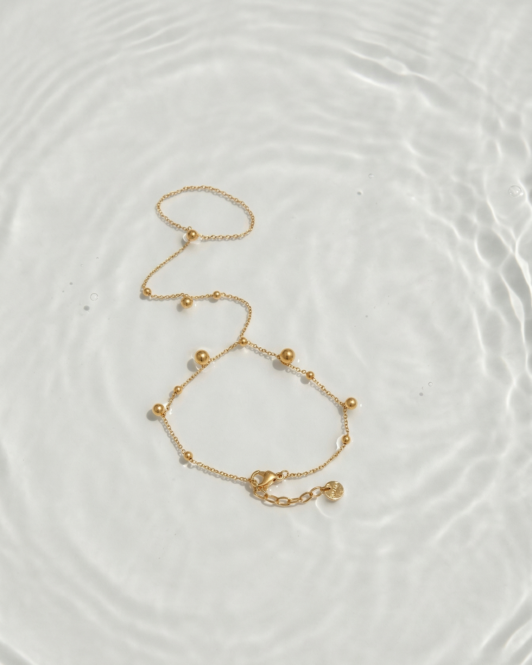 Gold bracelet on a white surface with water reflections