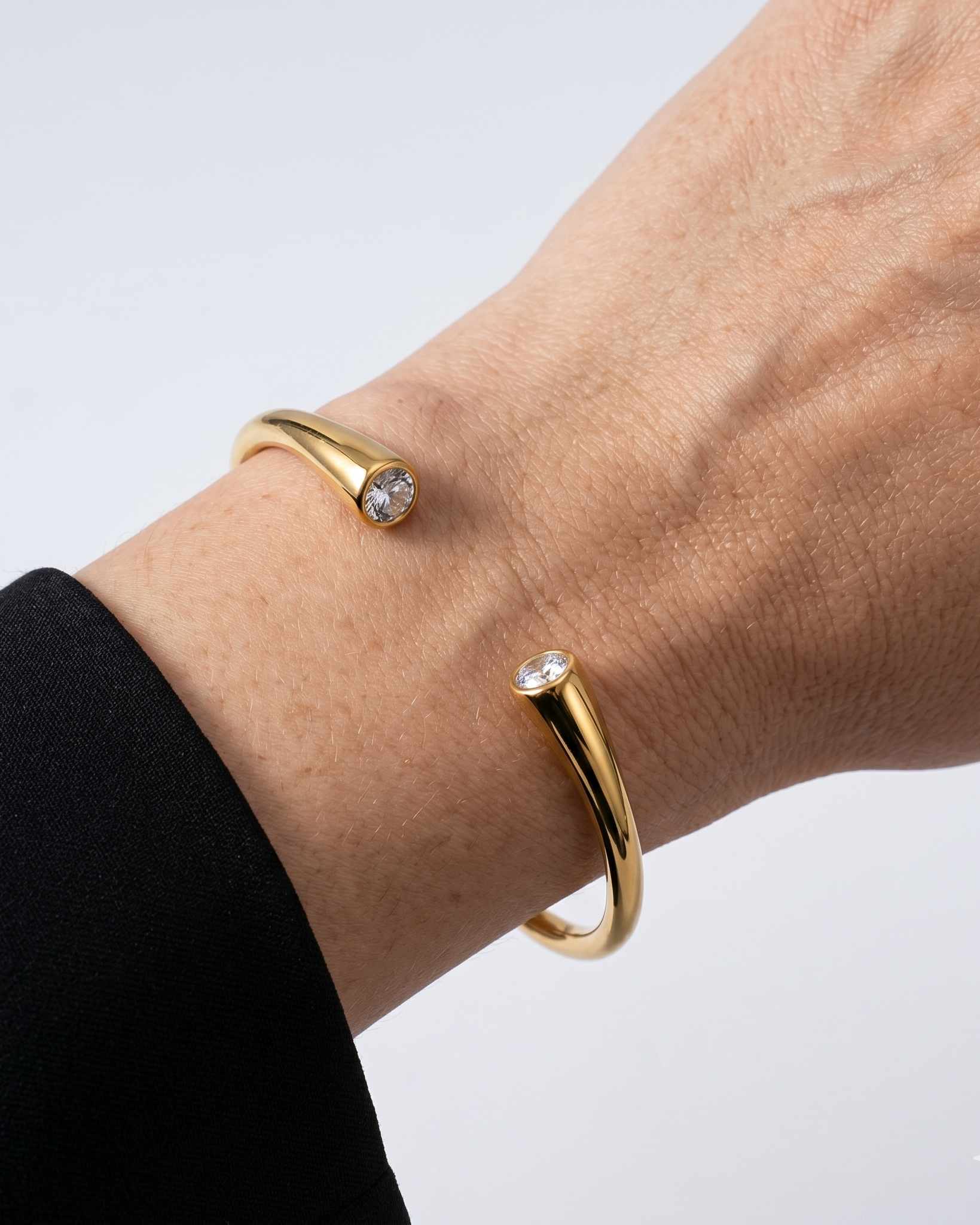 Gold bangle with a small gemstone on a wrist against a light gray background
