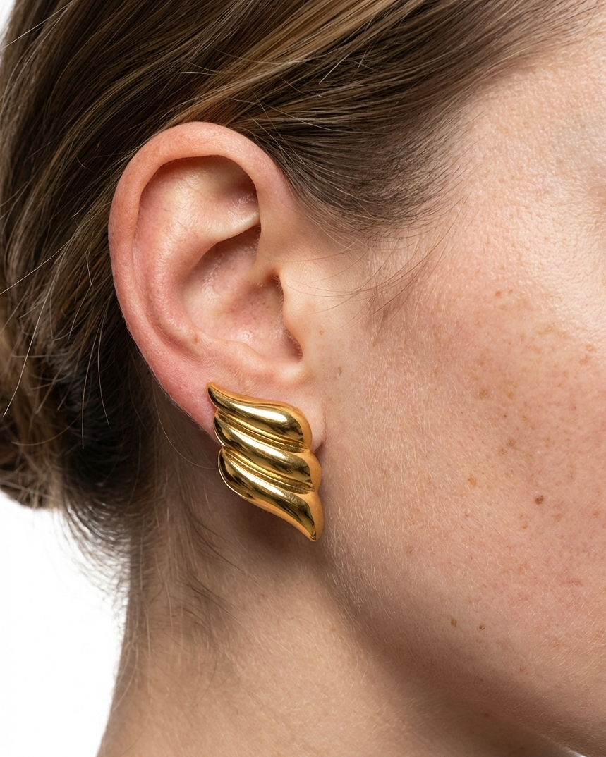Gold wing-shaped earring worn by a person on a white background