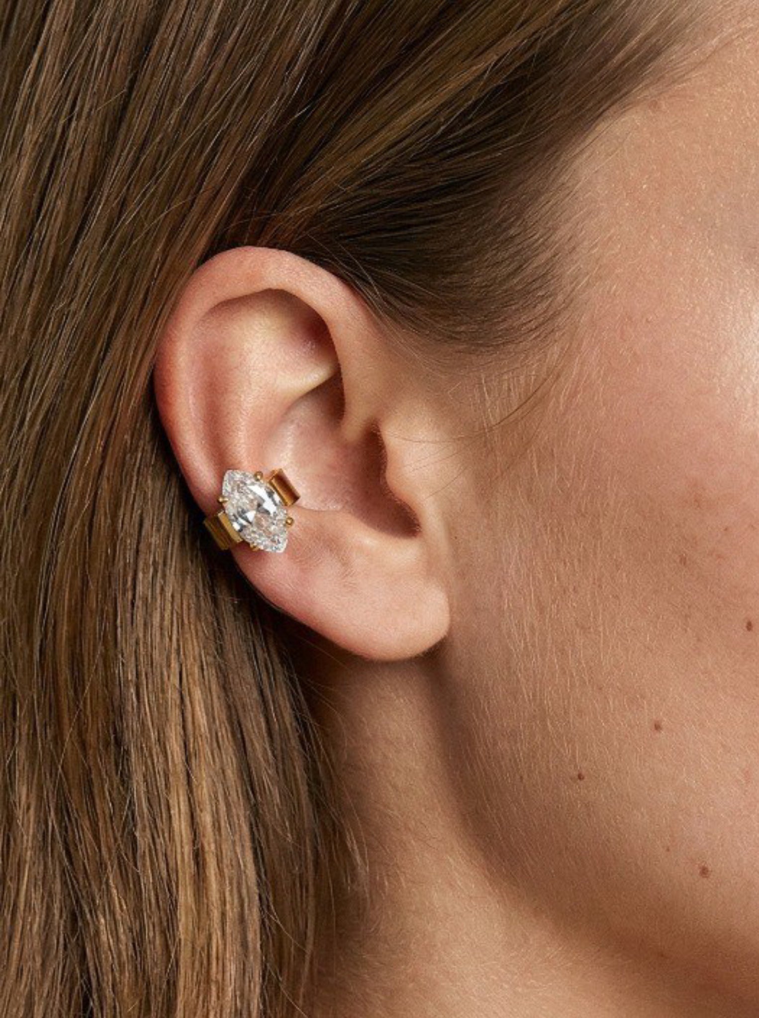 Close-up of an ear wearing a diamond earring with hair partially covering the frame.